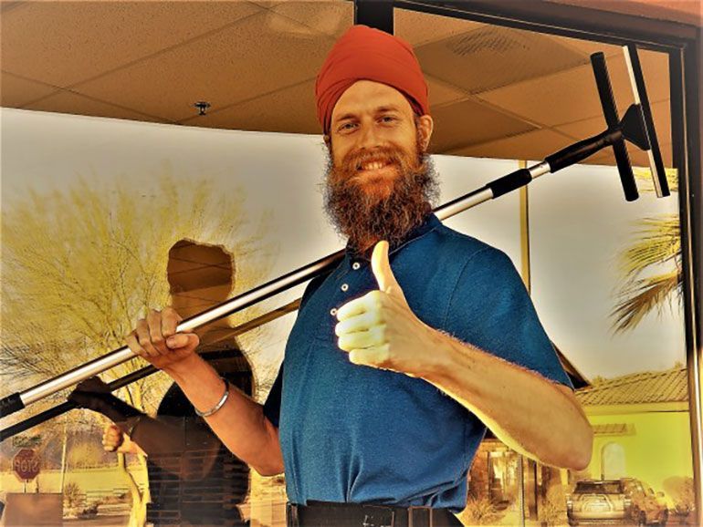 A man with a beard is holding a window cleaner and giving a thumbs up