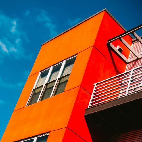 An orange building with a balcony and a blue sky in the background