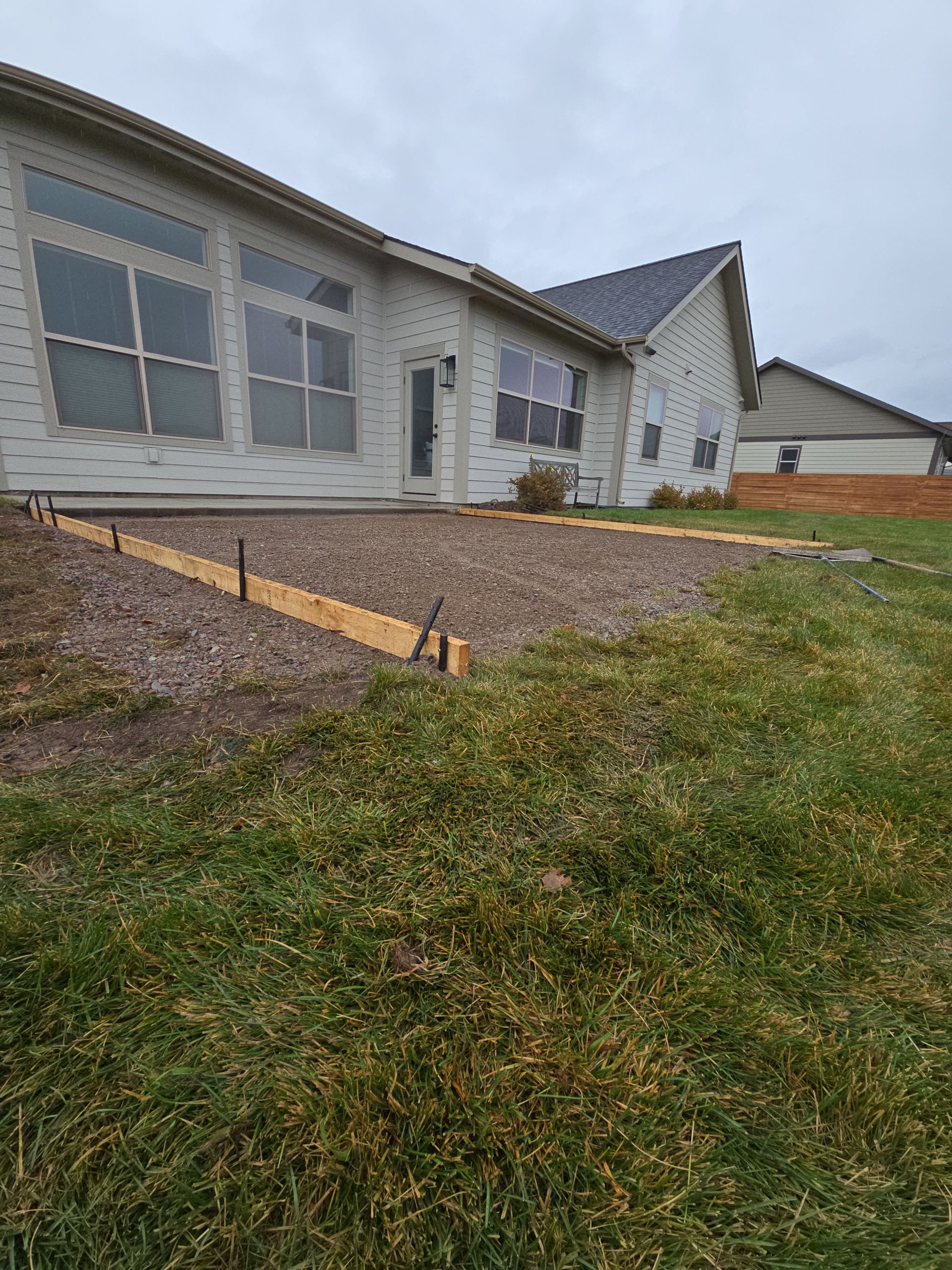 A gravel patio area prepared for concrete pouring with wooden formwork against the side of a house.