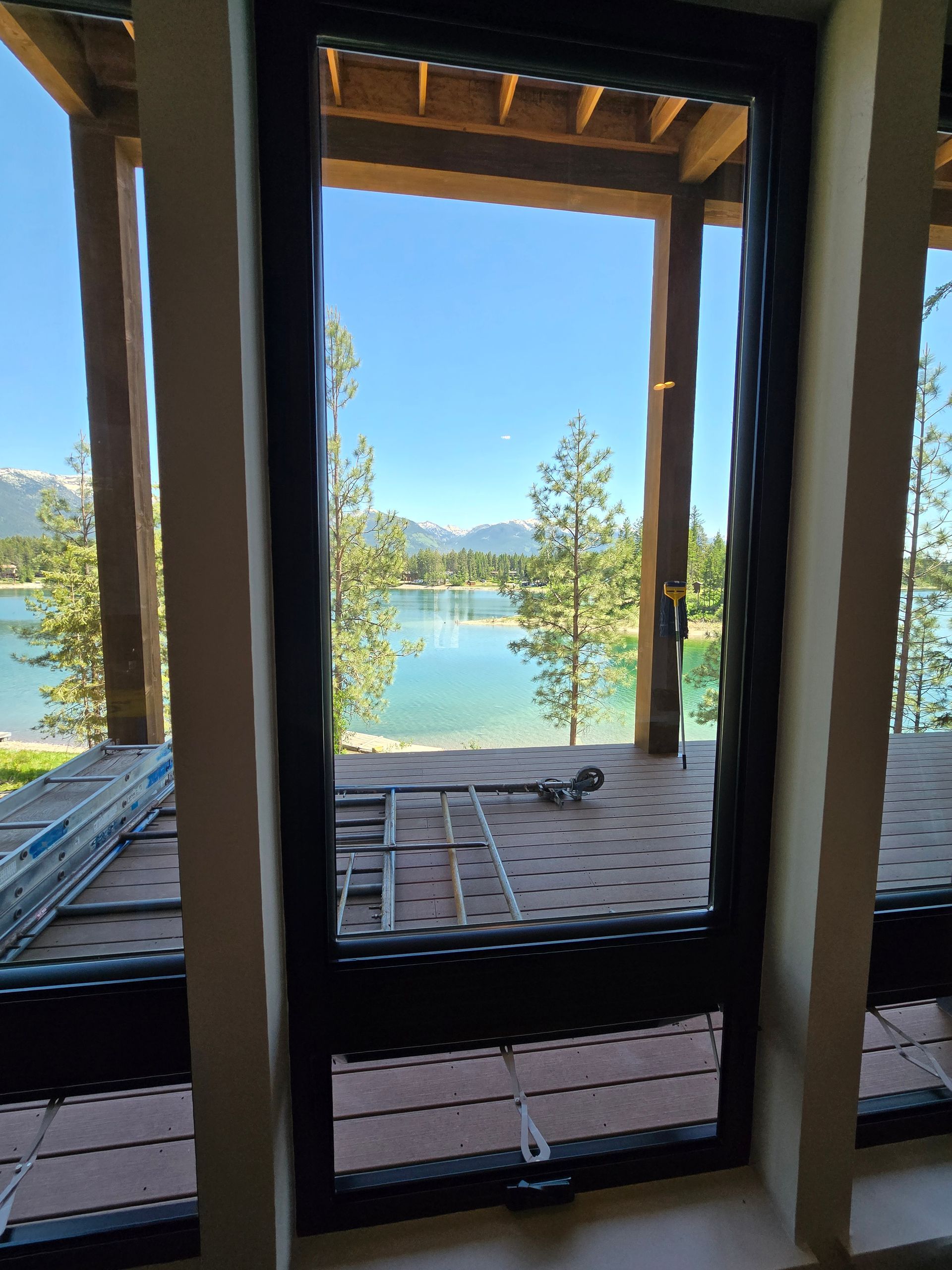 View of a serene lake and mountains through a modern, dark-framed window from an unfinished deck.