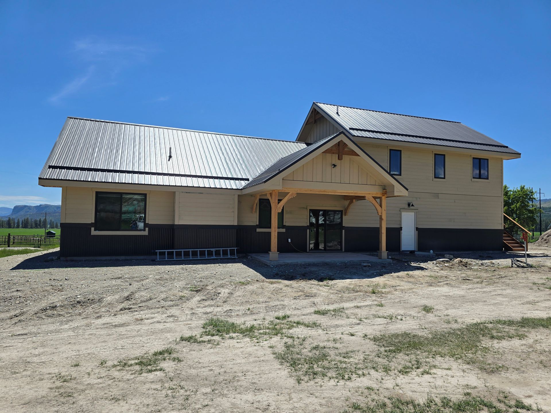 A newly constructed two-story house with tan siding, dark brown lower trim, a metal roof, and a timber-framed porch.