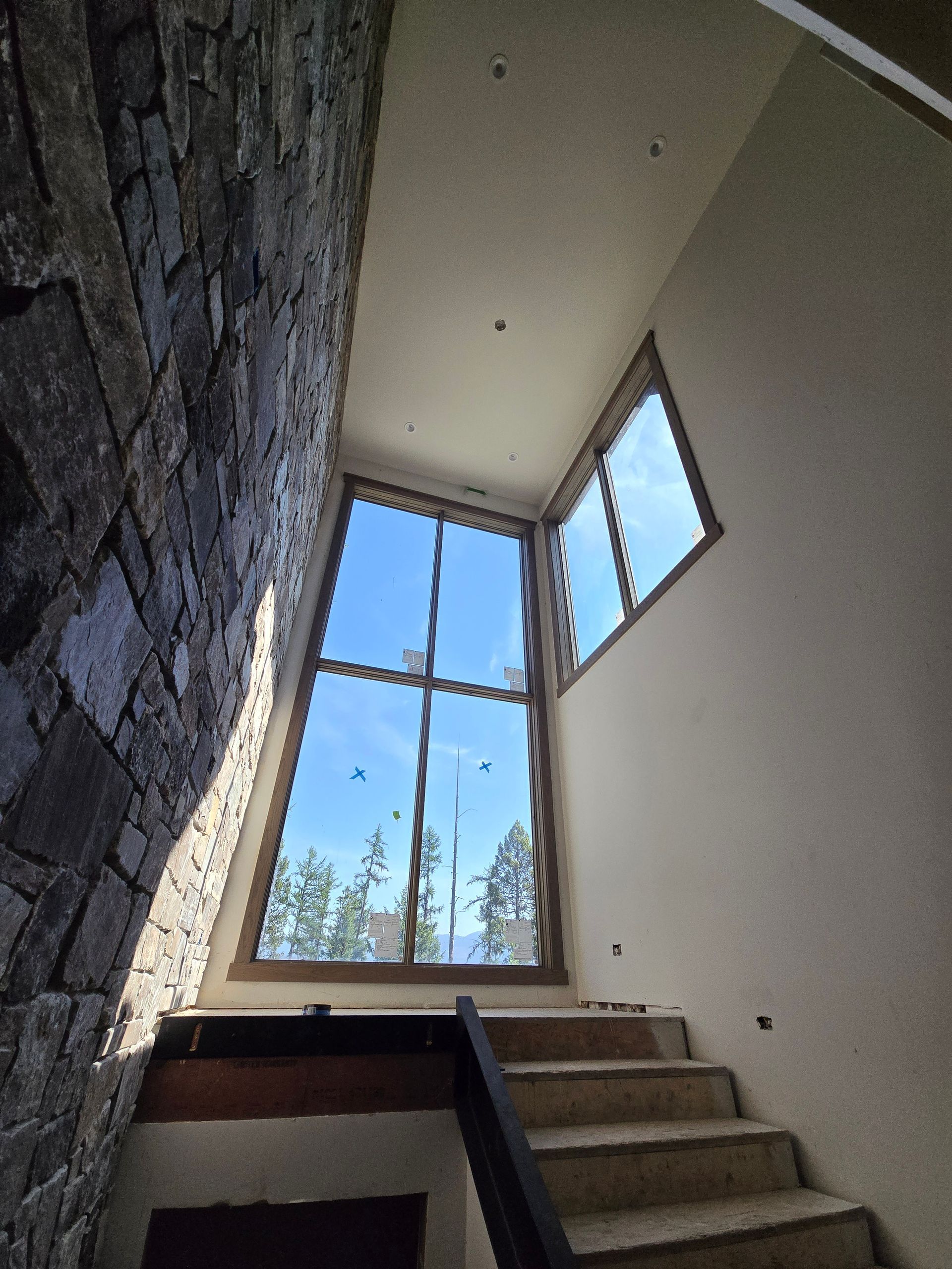 A tall, wooden-framed window in a stairwell, featuring a stone feature wall and beige plaster walls under a blue sky.