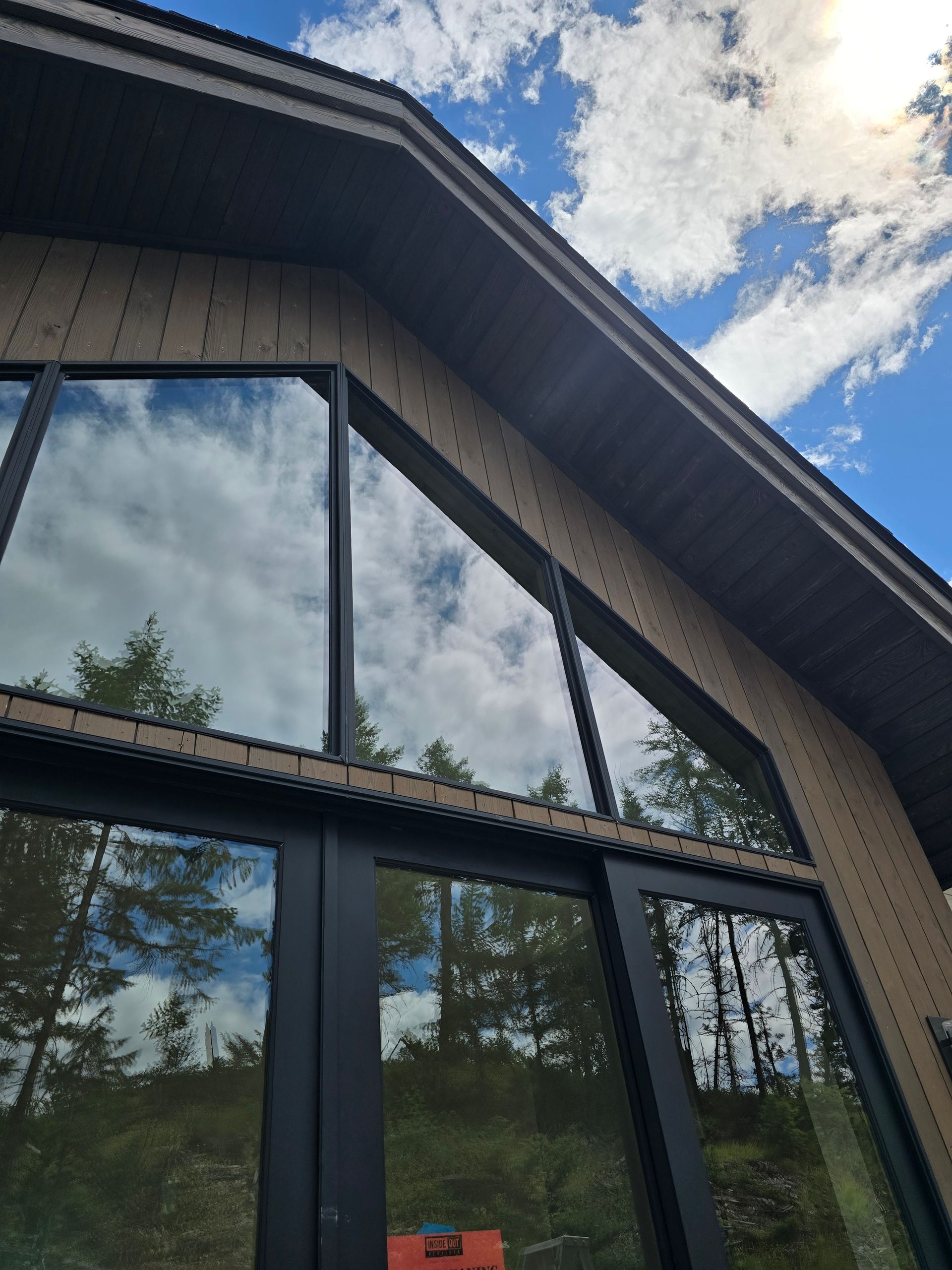 A close-up, low-angle view of a dark wood-paneled building exterior with tall, angled windows reflecting a cloudy sky.