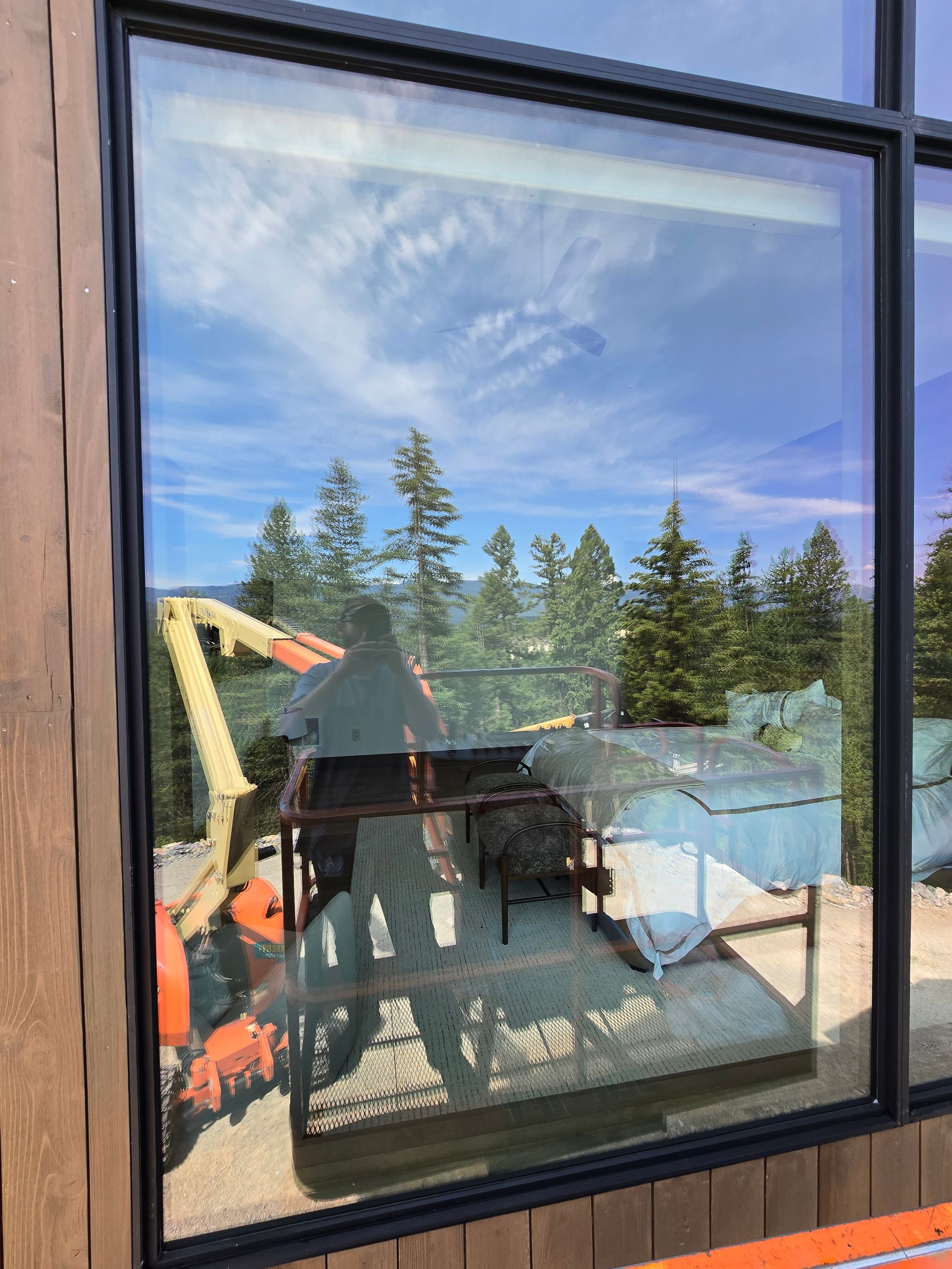 An orange construction lift reflecting in a large window with a forest view in the background.