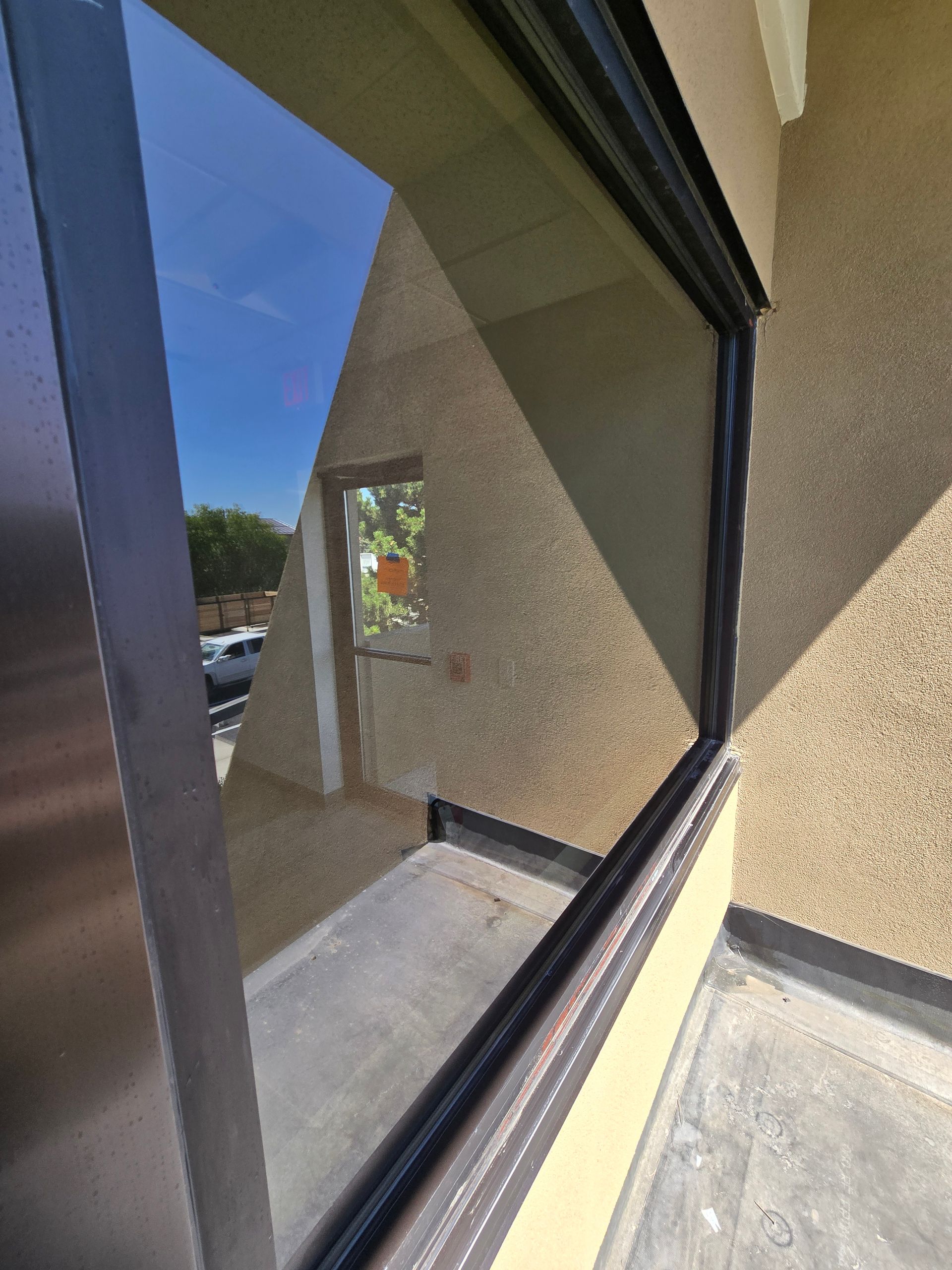 A view through a window showing a reflection of a beige building exterior and a glimpse of a parking lot outside.