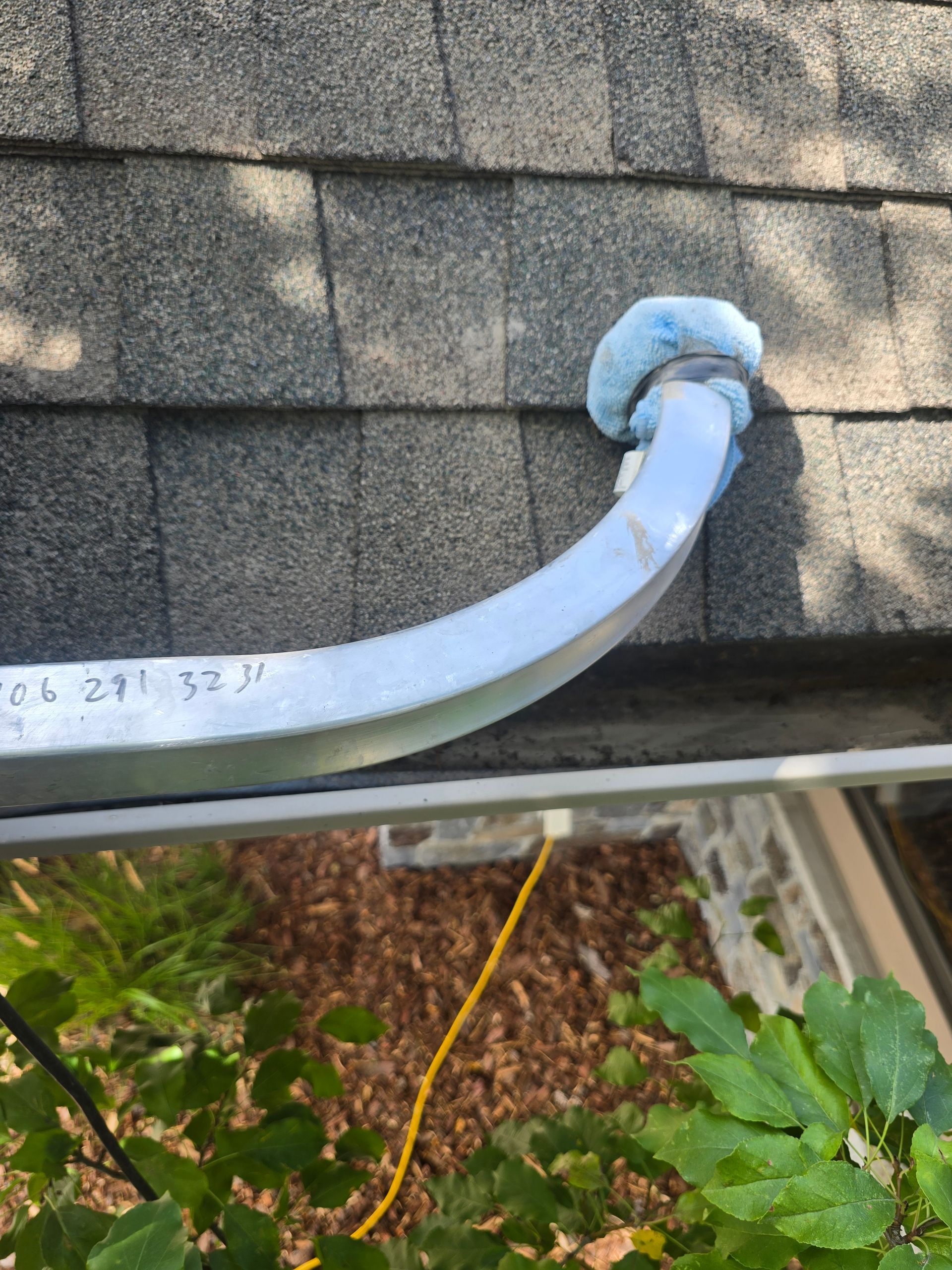 A metal ladder stabilizer with blue foam pads rests against a dark gray asphalt shingle roof.