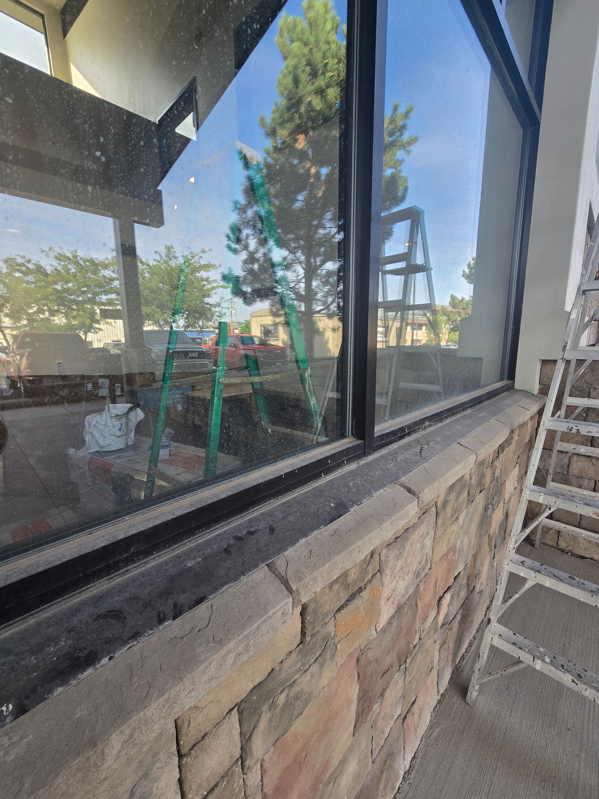 A low-angle view of a construction site showing a glass window being installed on a stone exterior wall with a ladder.