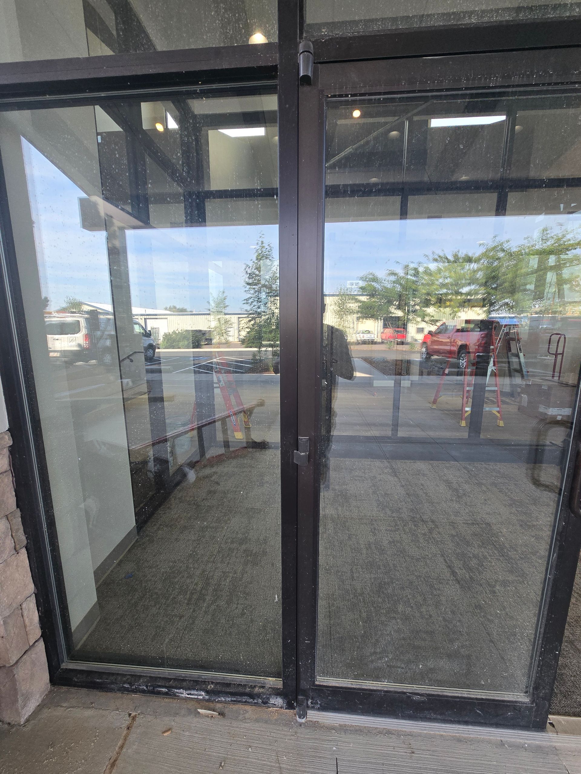 A pair of glass-paned doors with dark frames, showing a reflection of a building exterior and a red car parked outside.