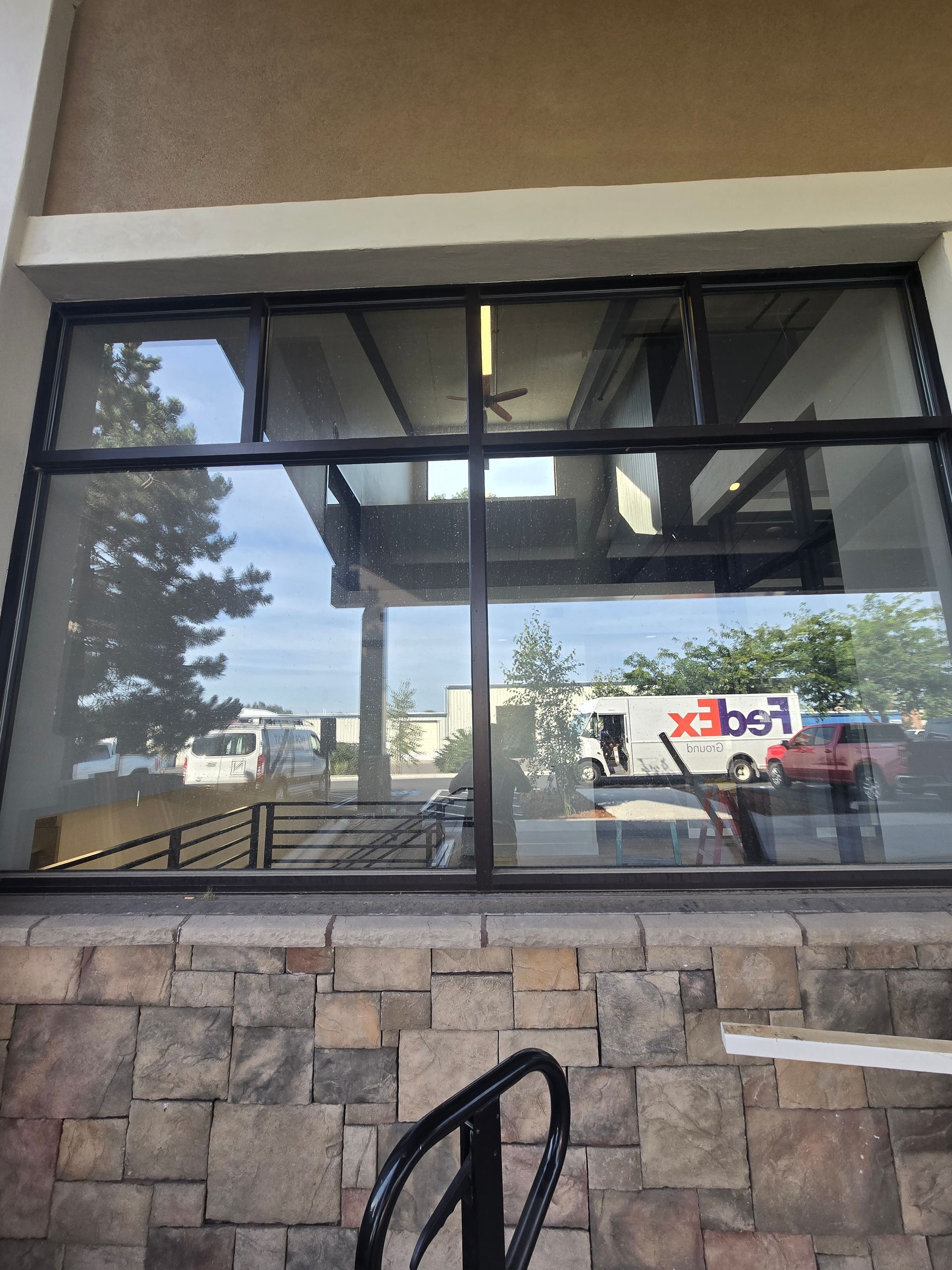 A stone-walled exterior viewed through a large window, reflecting a FedEx truck parked in a sunny parking lot.