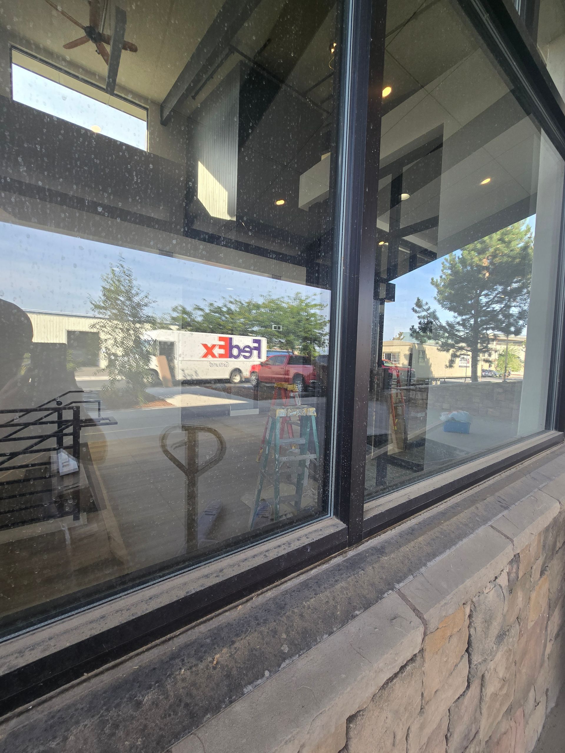 A FedEx truck is visible through a glass storefront window, reflecting the outdoors in front of a stone-faced building.