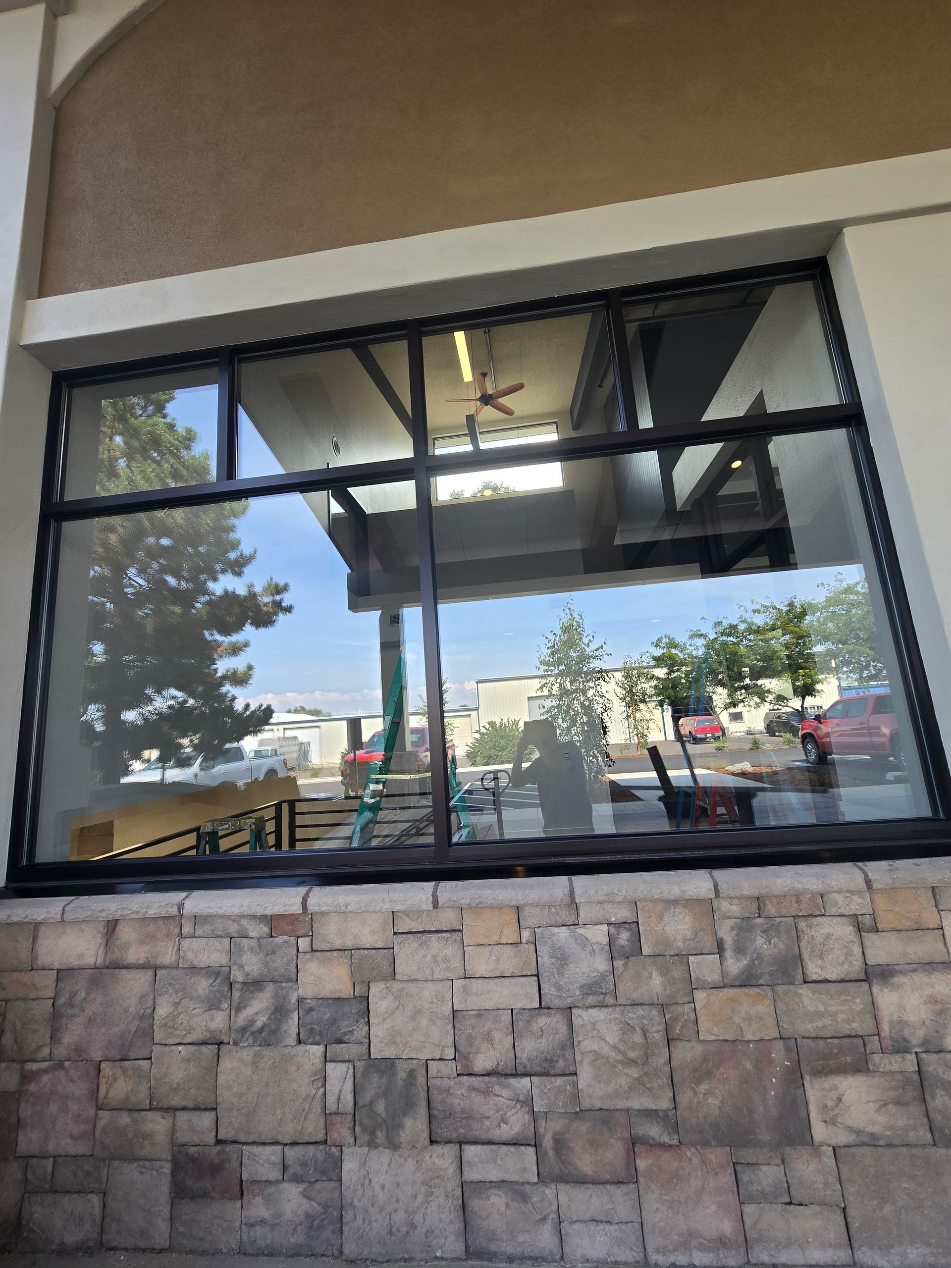 A large, multi-pane rectangular window set into a stone exterior wall, reflecting the surrounding trees and parking lot.