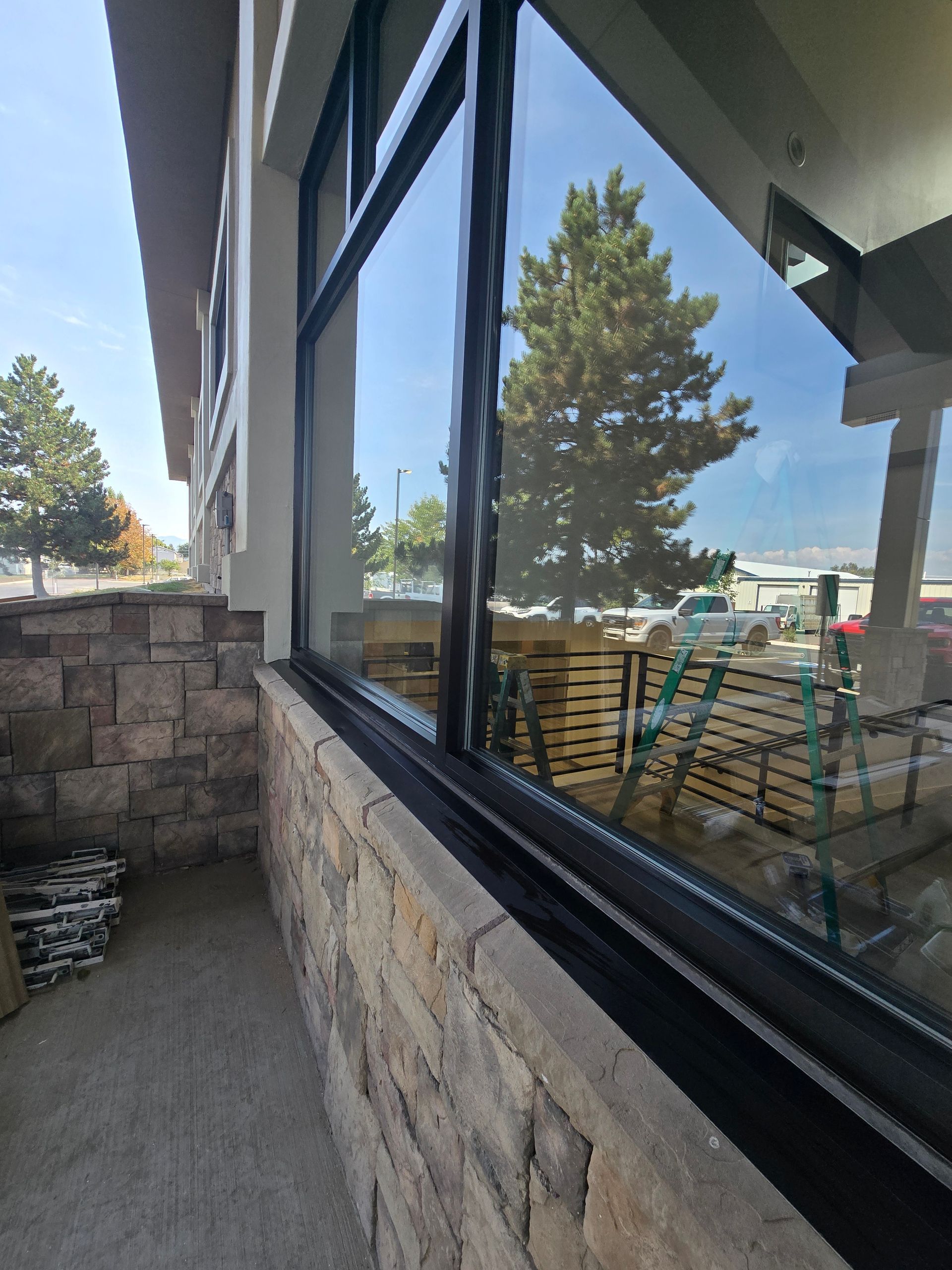 A stone-walled exterior wall with a large black-framed window reflecting a sunny parking lot and trees.