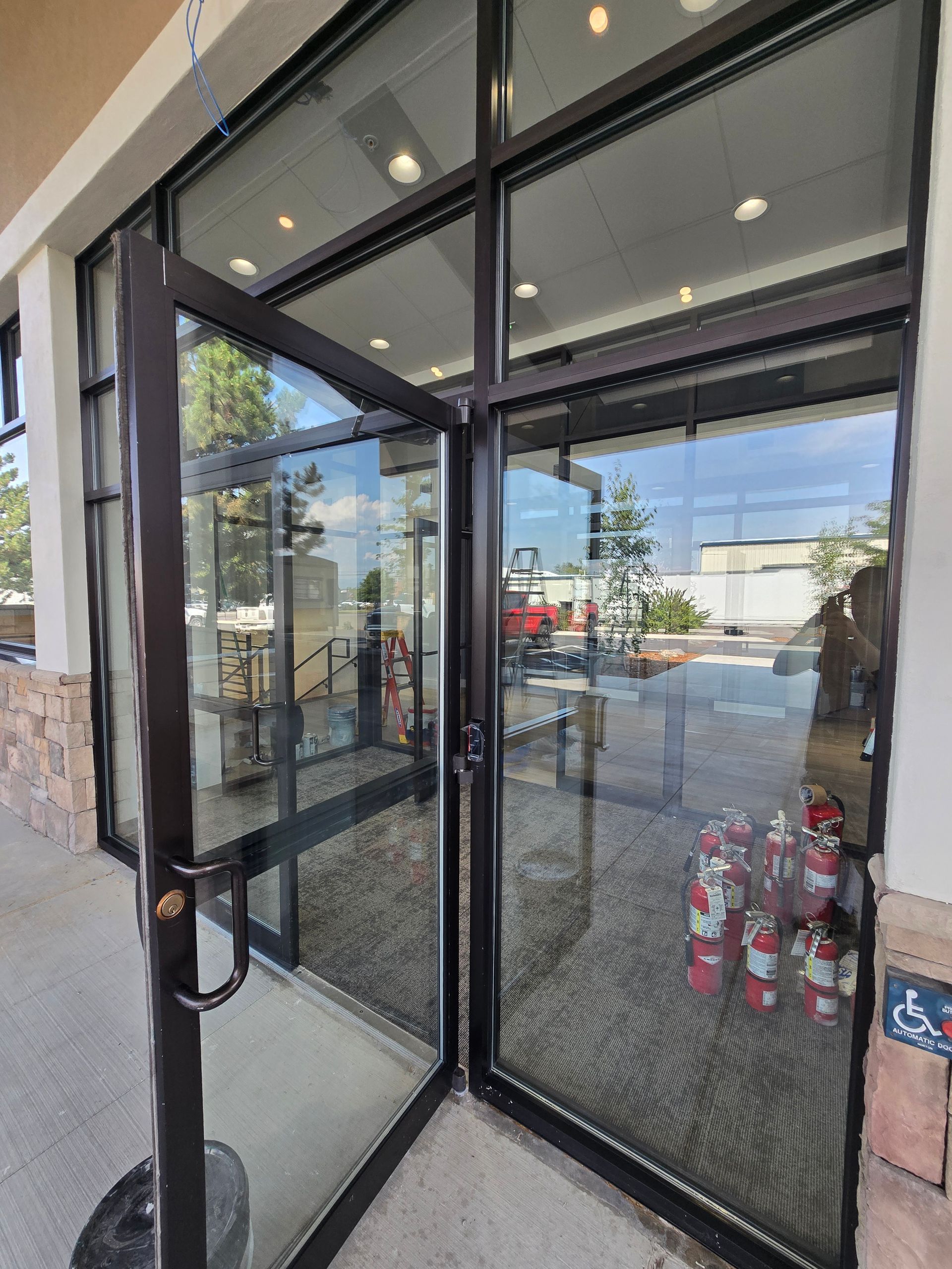 A partially open glass storefront door with a black metal frame at a building entrance.