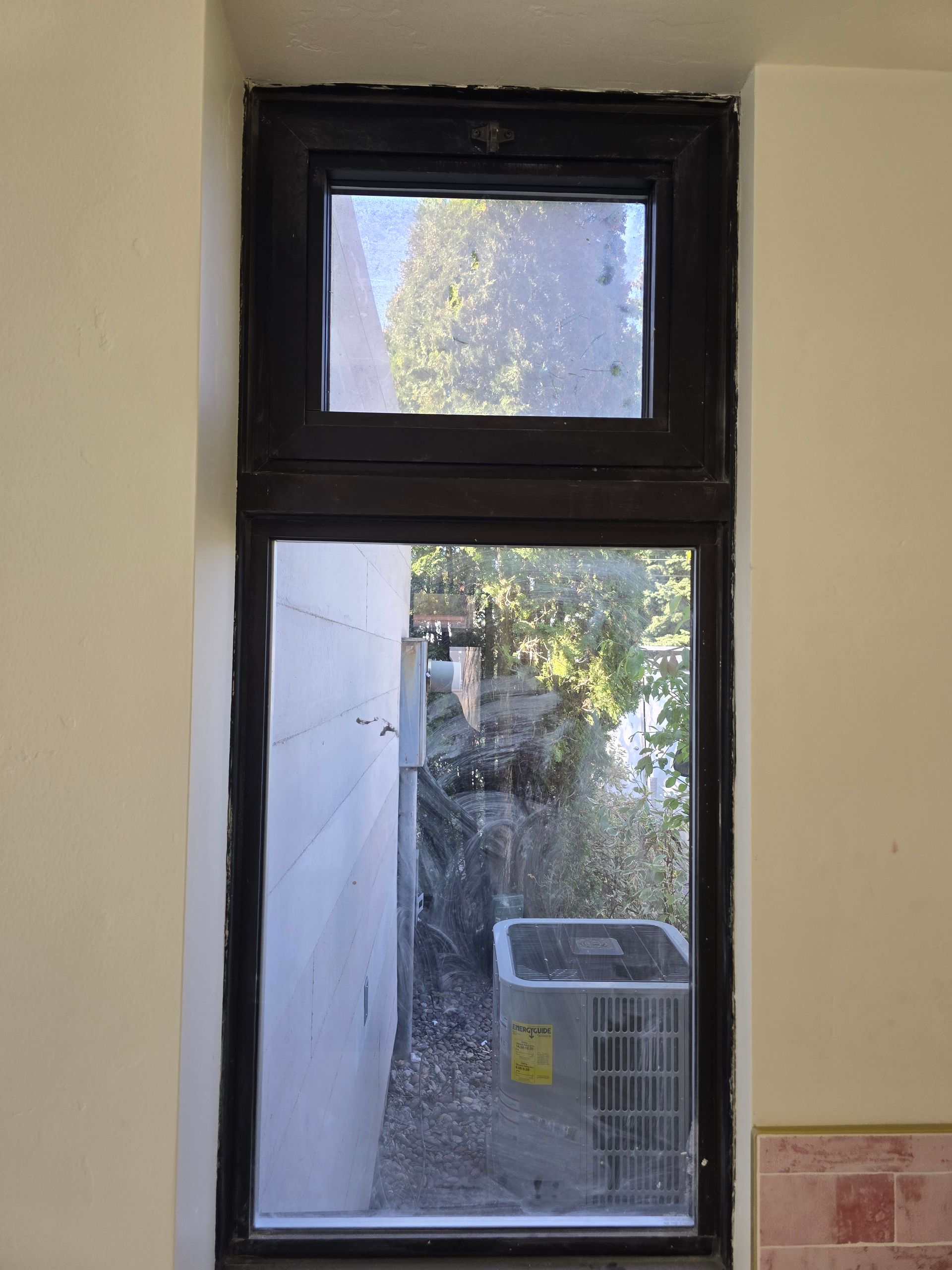 A rectangular window with a black frame divided into two sections, showing an outdoor view of a building and AC unit.