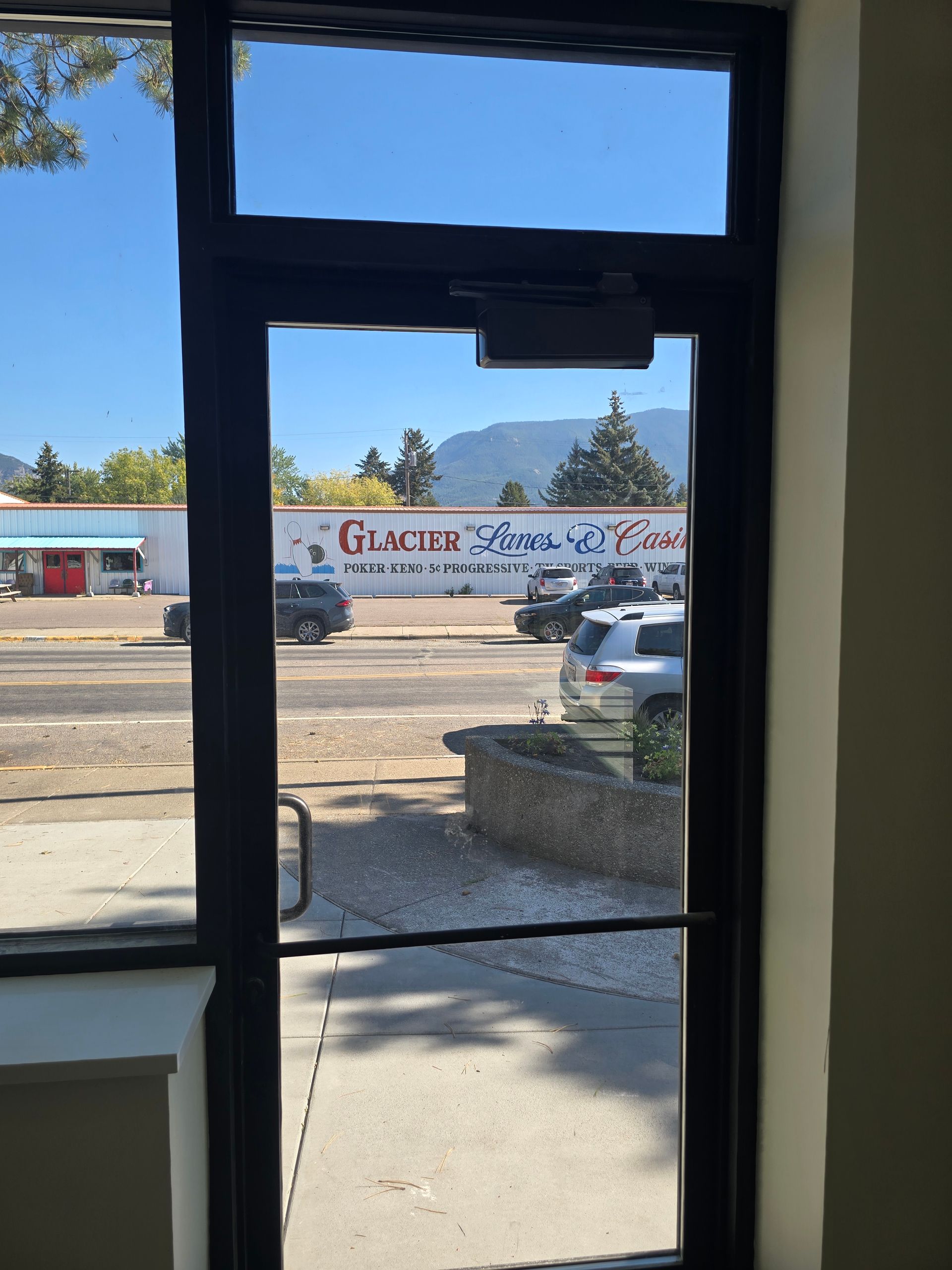 View through a glass door looking out at a street with cars and a building labeled 
