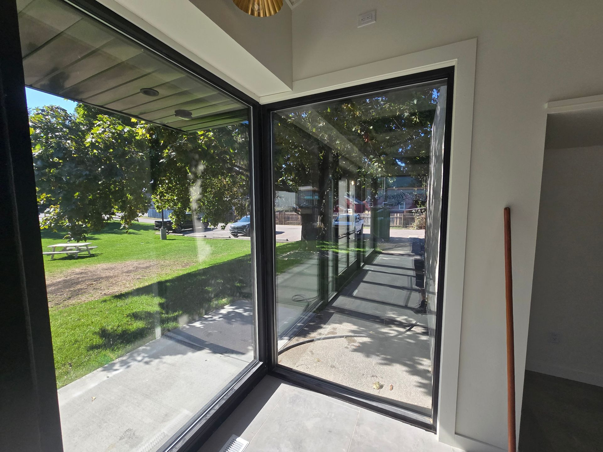 Interior view of floor-to-ceiling glass corner windows looking out onto a sunny yard and a shaded walkway.