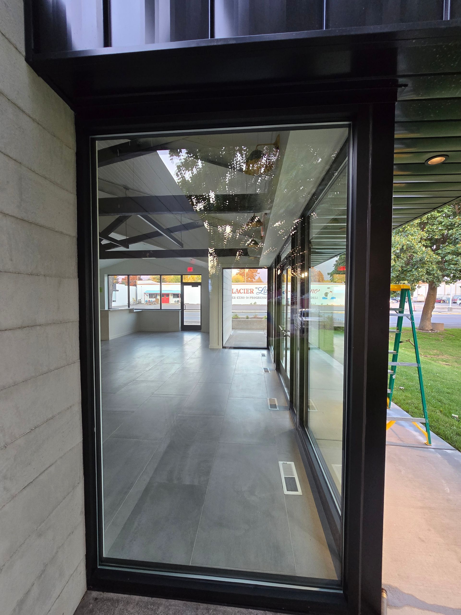 A view through a floor-to-ceiling glass storefront into a modern, empty commercial space with a black metal frame.