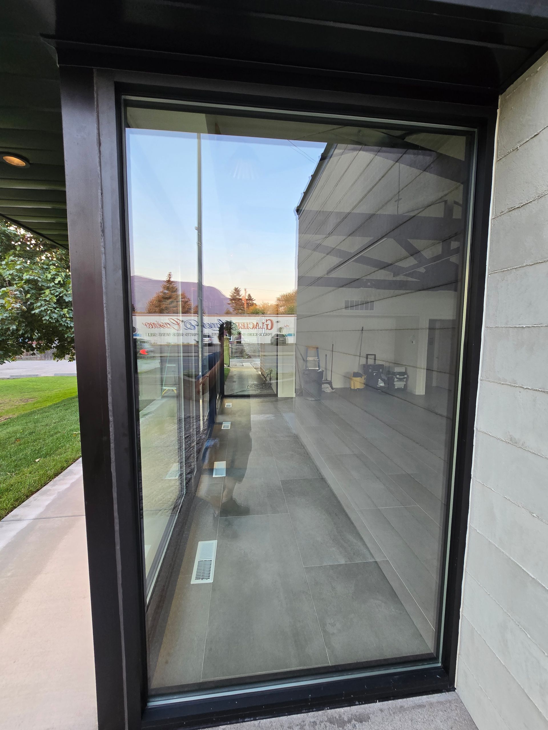 A glass storefront window looking into an empty retail space with dark flooring and a view of trees and sky outside.
