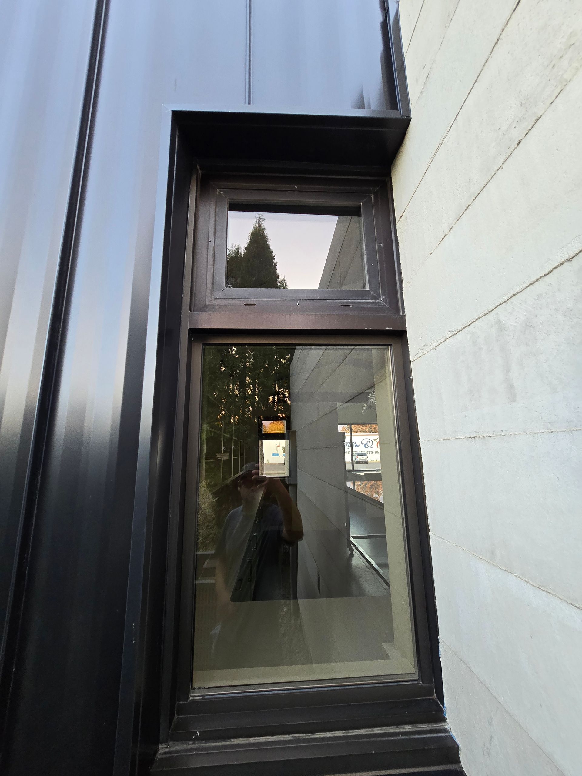 A rectangular window with a smaller top pane and larger bottom pane, set between a black metal wall and a white wall.