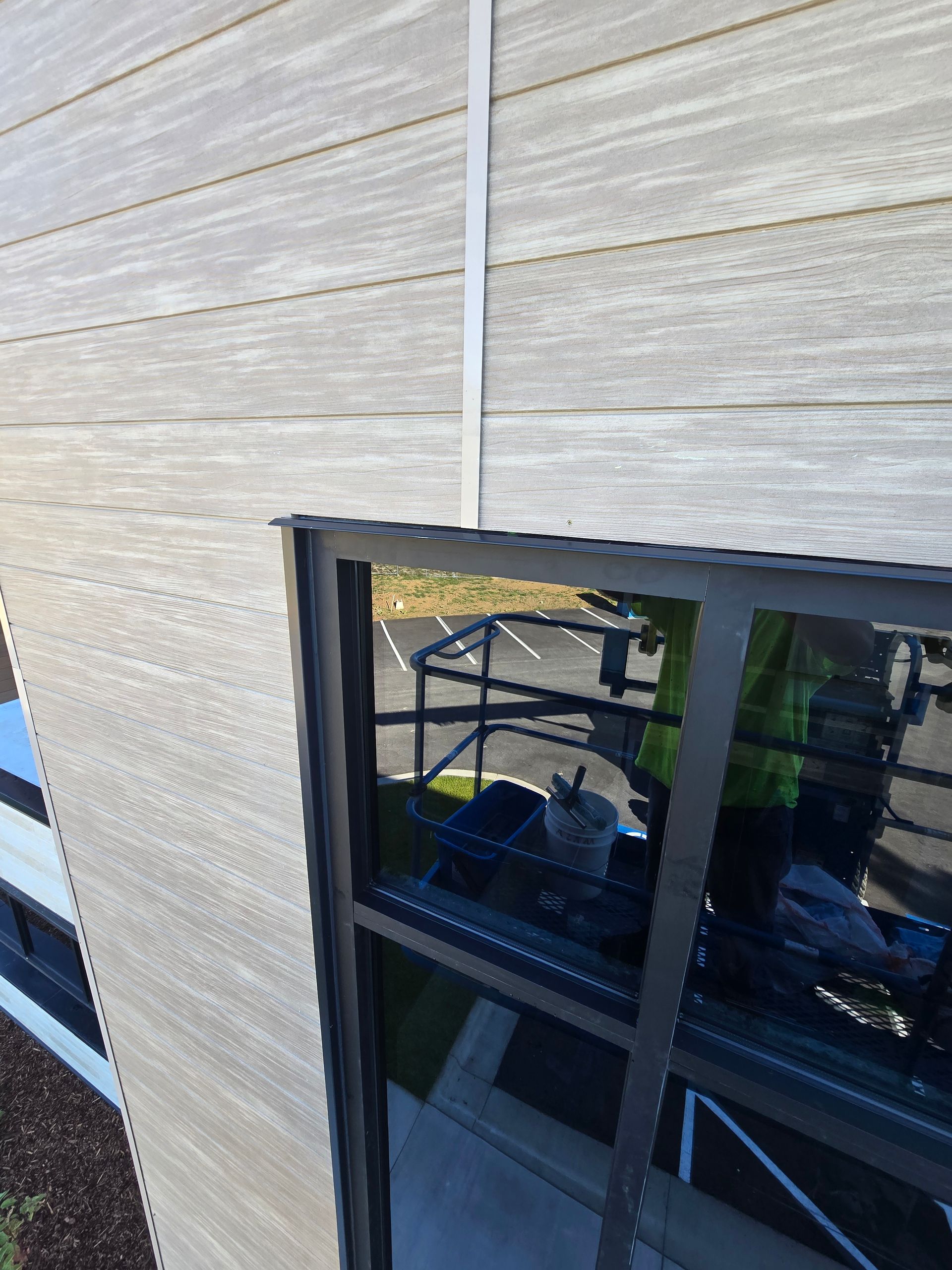 A worker in a high-visibility jacket is visible in the reflection of a newly installed window on a light-colored siding wall.