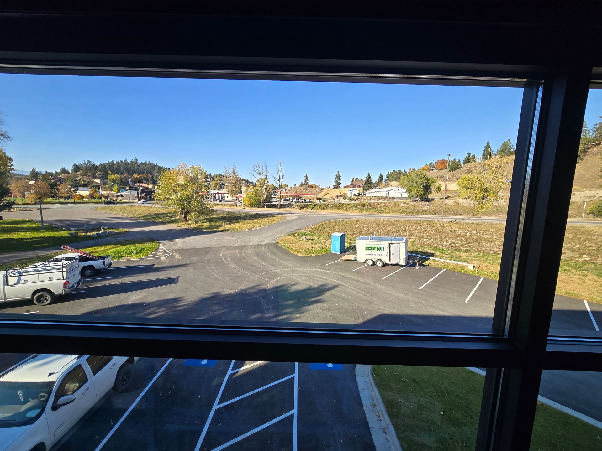An elevated outdoor view of a parking lot with several vehicles, a portable toilet, and a trailer under a blue sky.