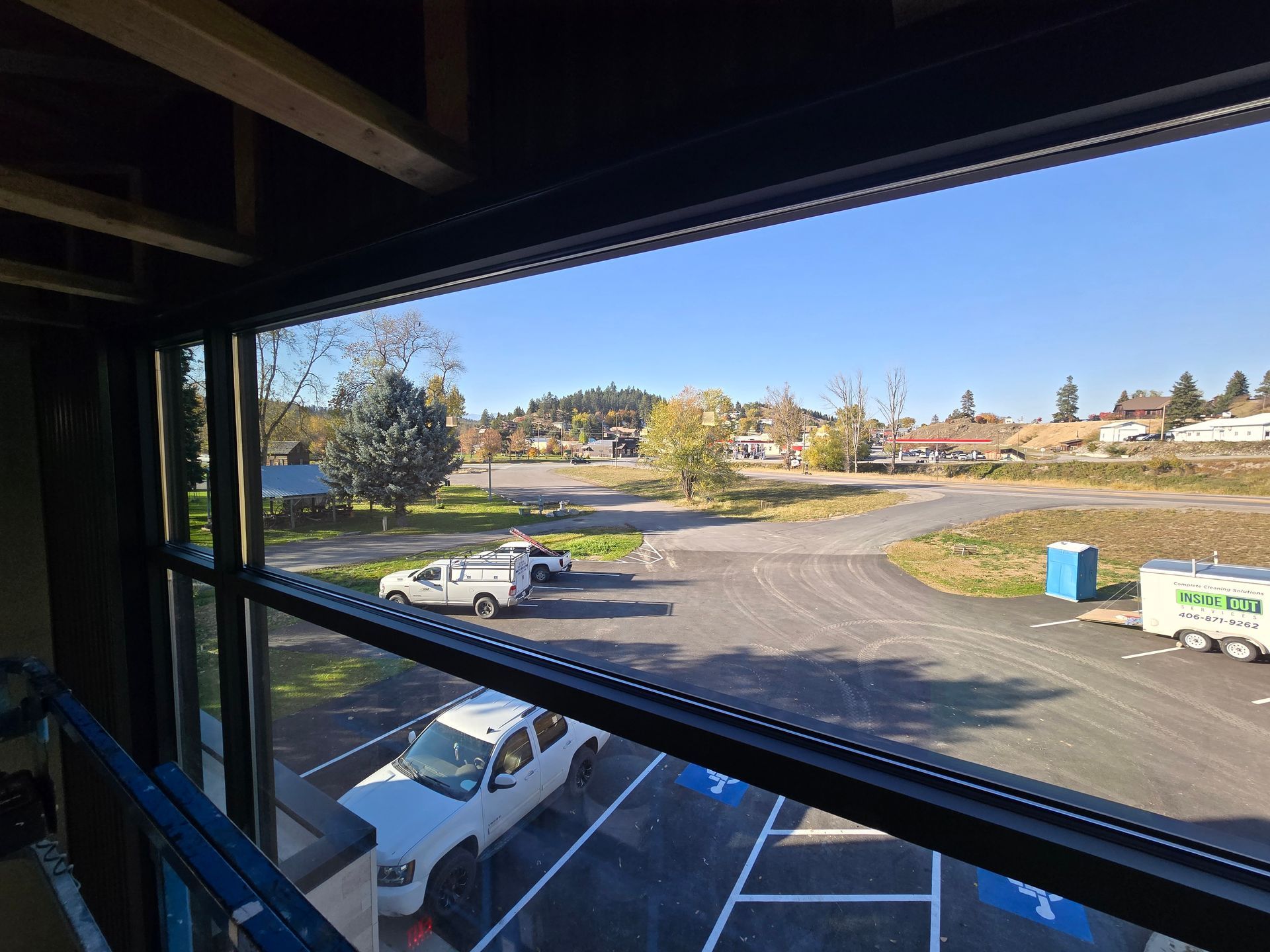 View from a window under construction, overlooking a parking lot with two white trucks and a blue portable toilet.