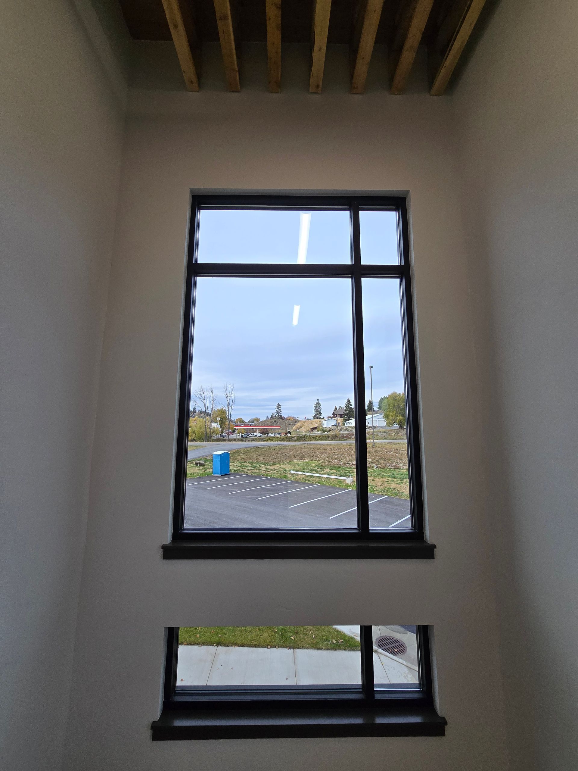 A tall, rectangular window stacked above a small, horizontal window in a white, minimalist room with wooden ceiling beams.