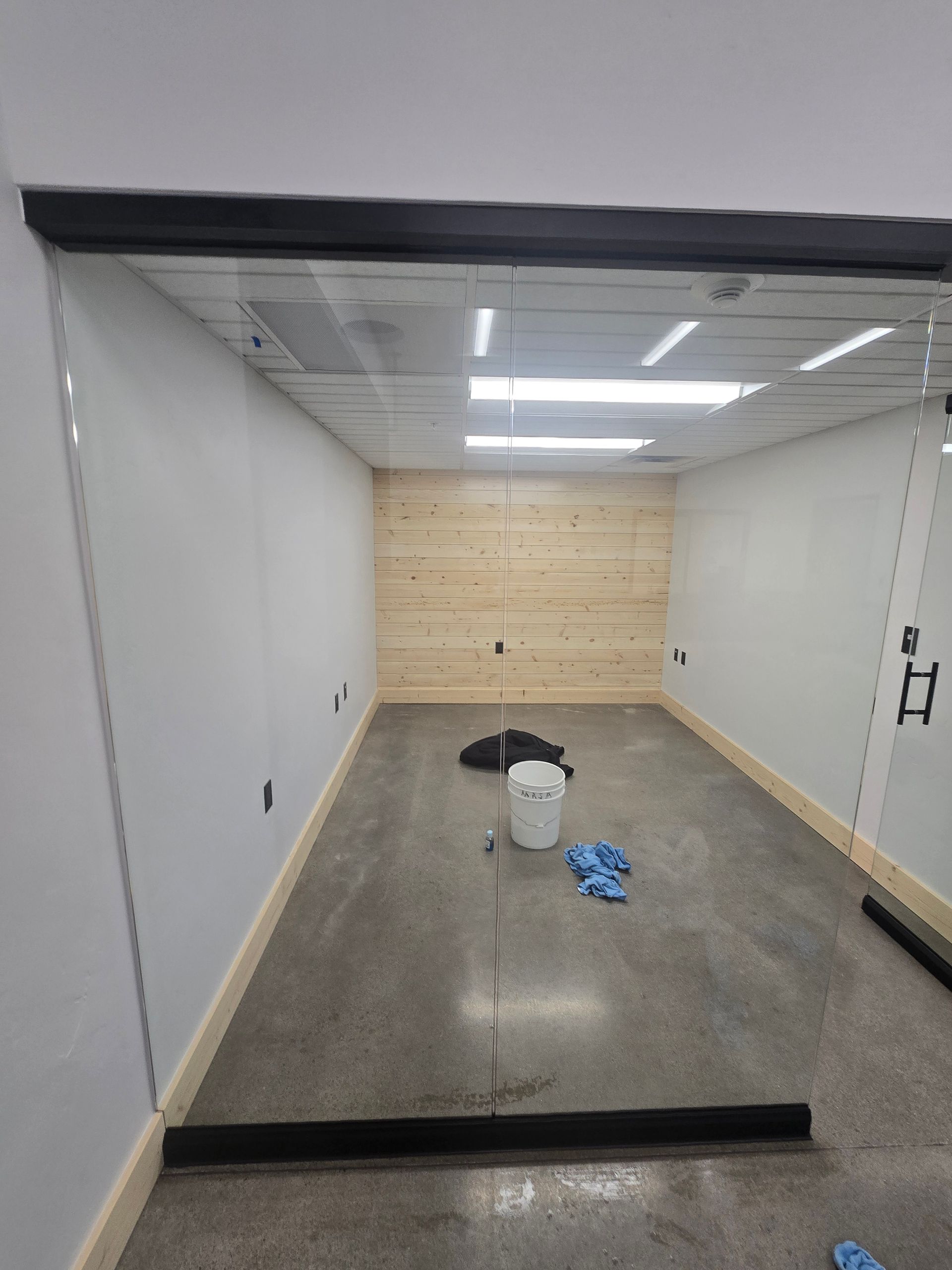 A small, rectangular room with gray concrete floors, white walls, and a wood-paneled back wall seen through glass doors.