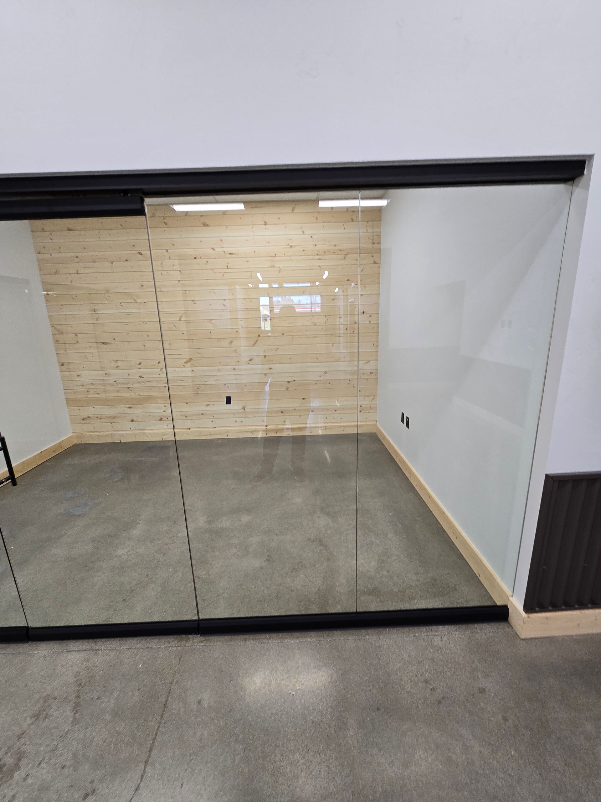 A glass-walled office with a light wood-paneled back wall and smooth, polished gray concrete floors.