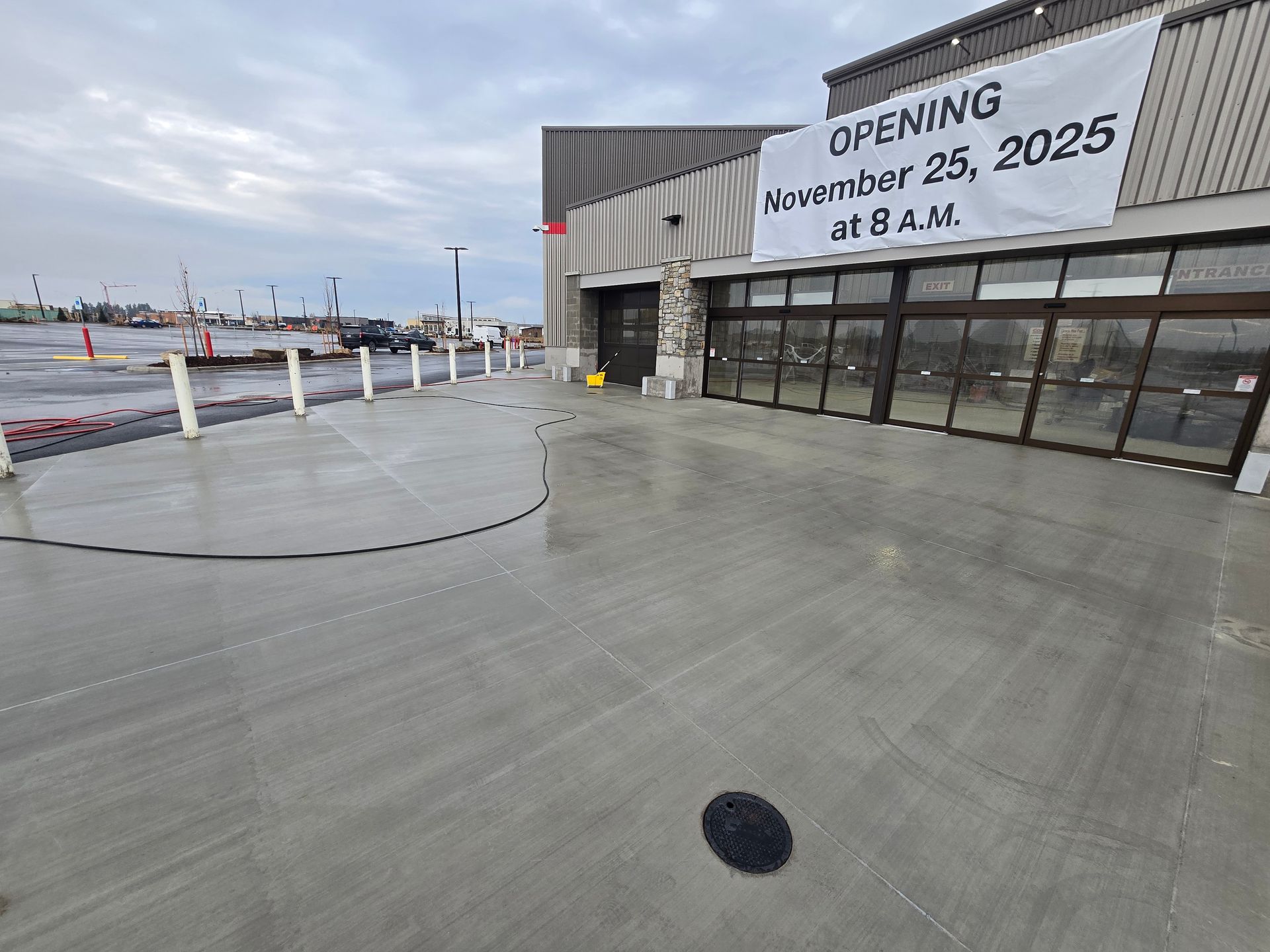 Newly paved concrete entrance of a building with a banner announcing an opening on November 25, 2025, at 8 A.M.