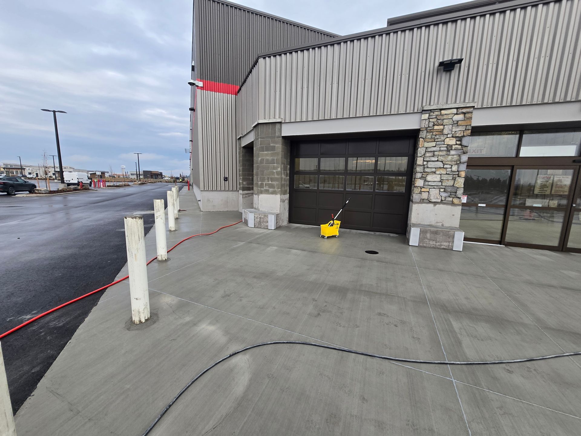 A yellow bucket sits on the sidewalk in front of a dark glass garage door at the entrance of a commercial building.