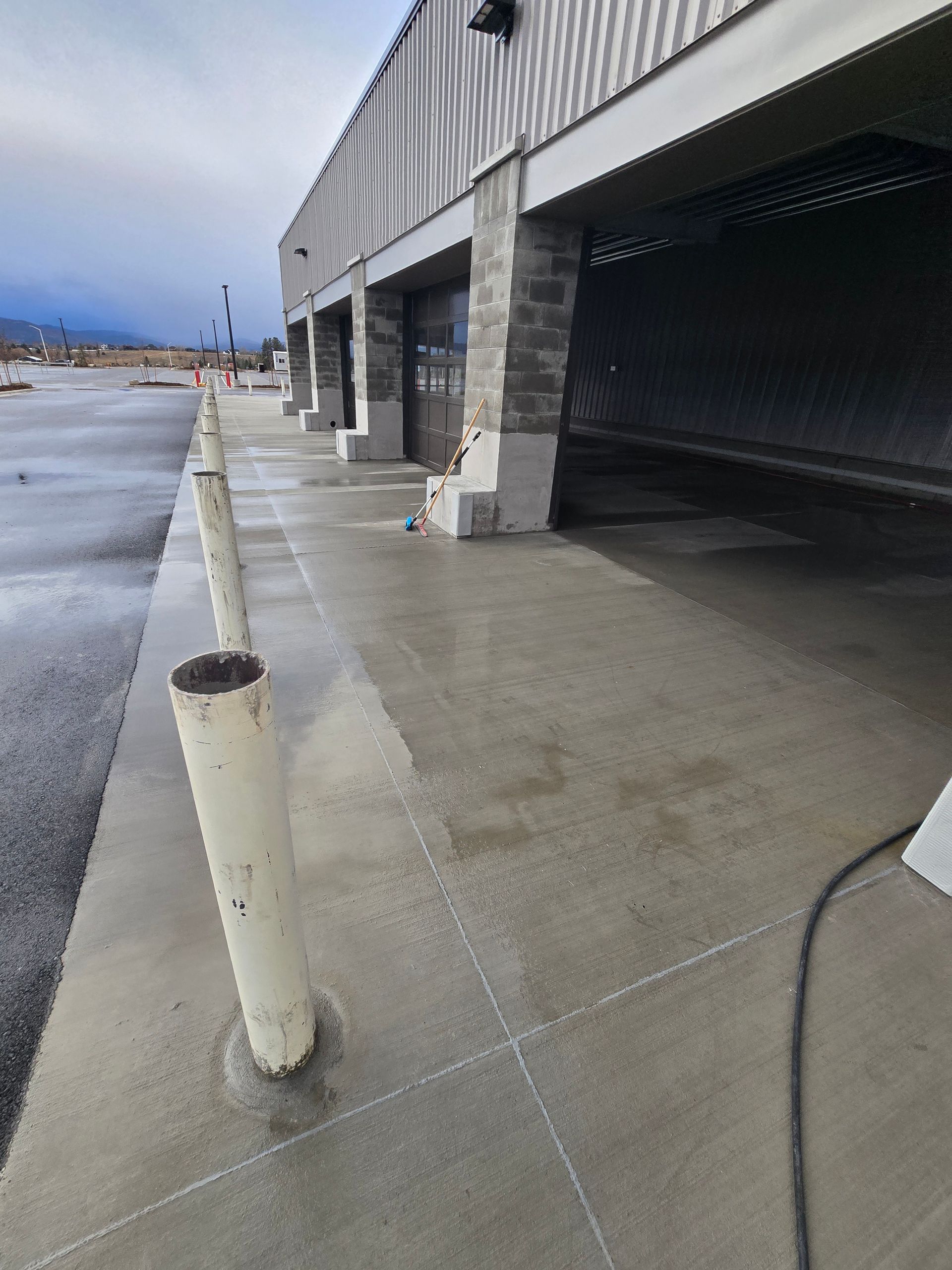 A row of white bollards lining a concrete sidewalk next to a building with stone pillars and a metal facade.