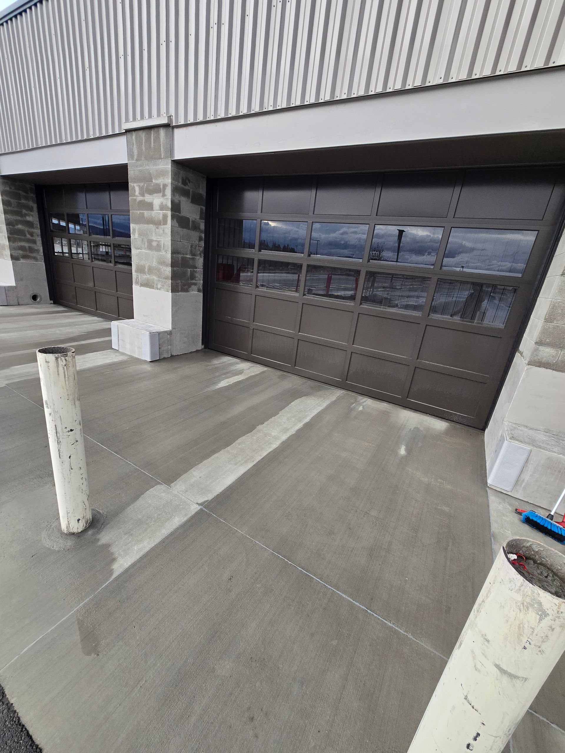 Two industrial glass garage doors on a building exterior with stone accents and two white safety bollards in front.