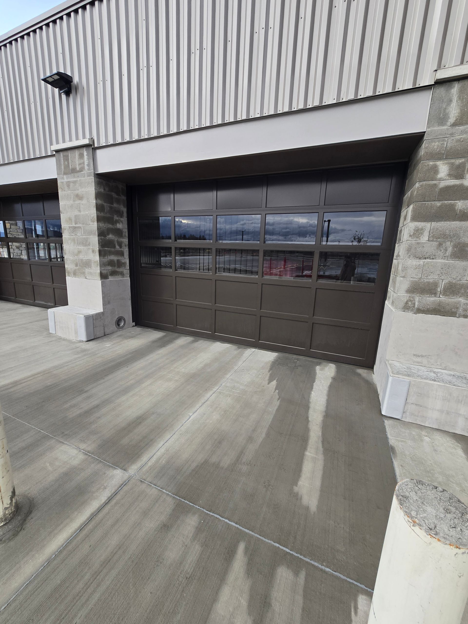 A building facade with two dark brown, glass-paneled industrial garage doors and a concrete walkway in front.