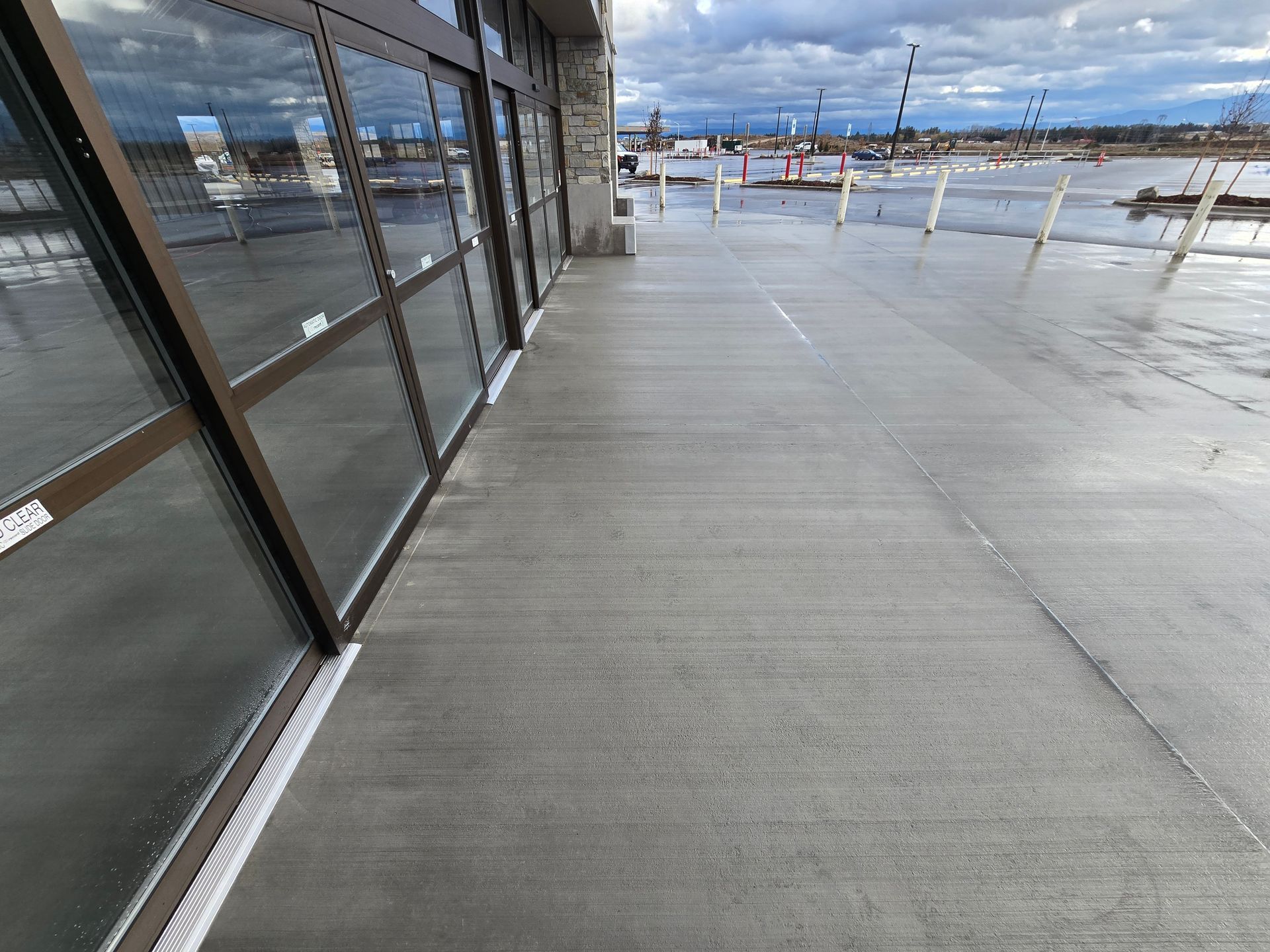 A wide concrete sidewalk stretches alongside a glass storefront under a cloudy sky.