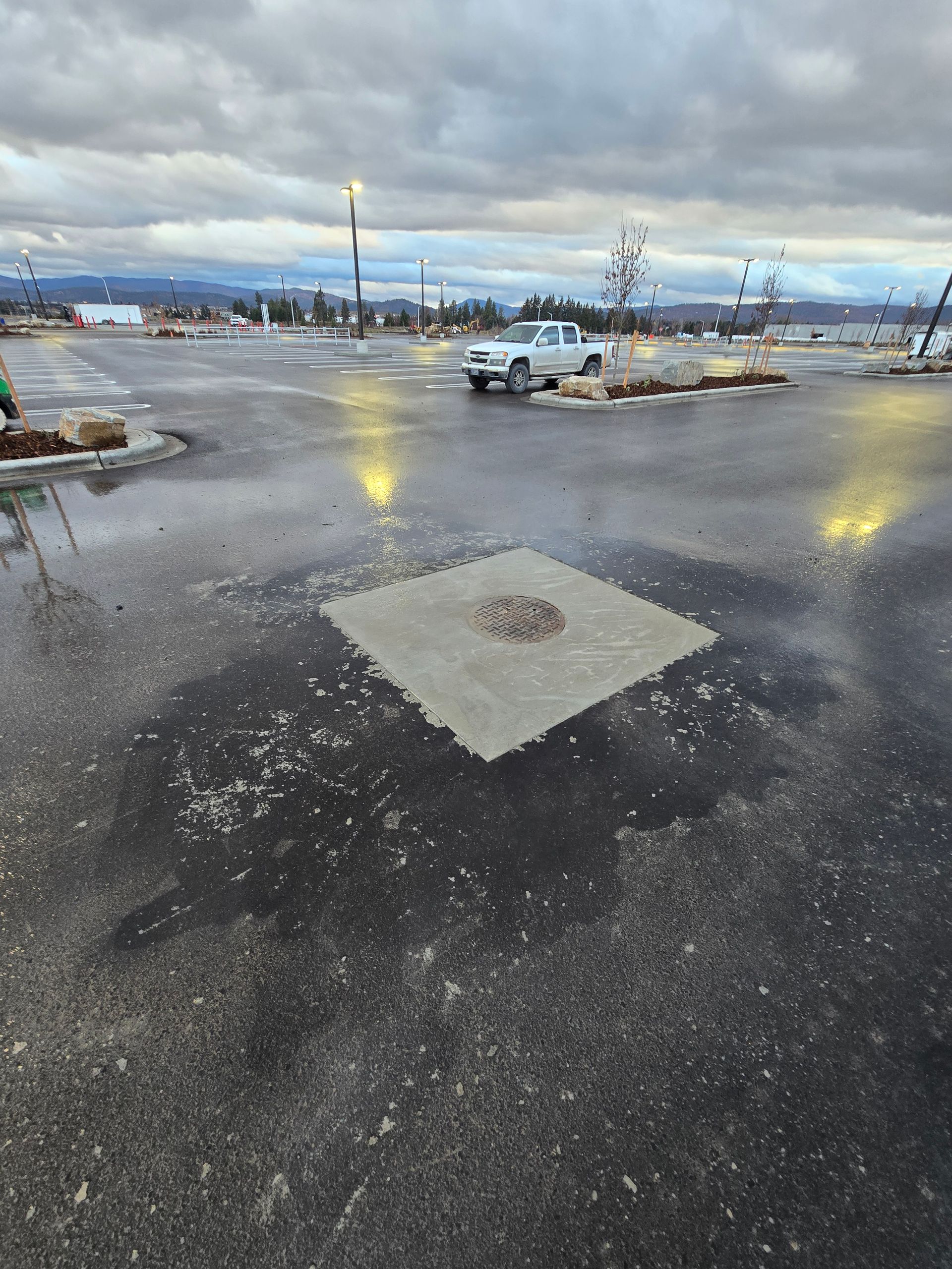 A patch of light-colored concrete in the middle of a dark, wet asphalt parking lot under a cloudy sky.