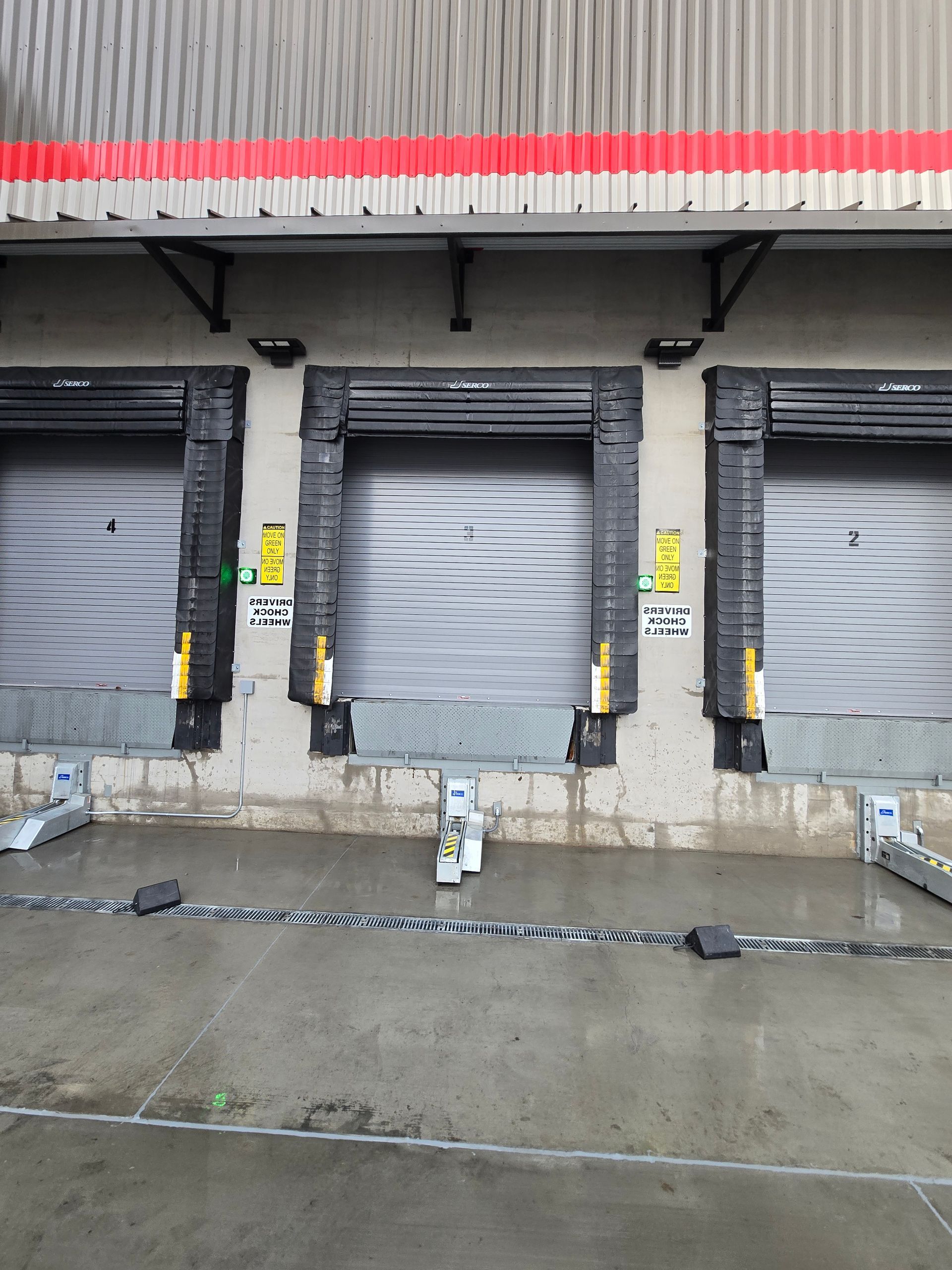 Three industrial loading dock bays with metal roll-up doors and black rubber seals on a concrete exterior wall.