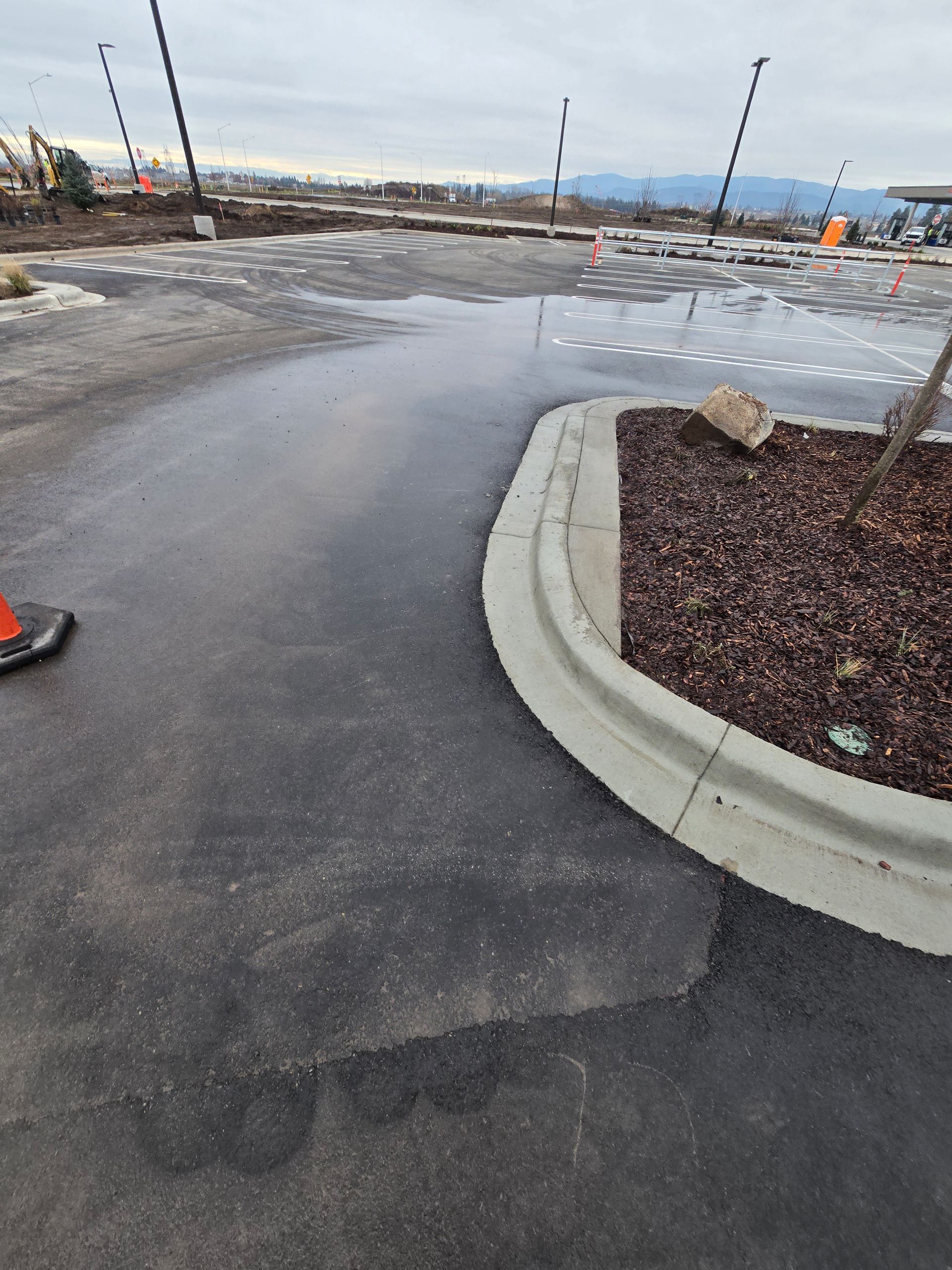 A parking lot with a paved surface, a landscaped curb area, and large puddles of standing water under an overcast sky.