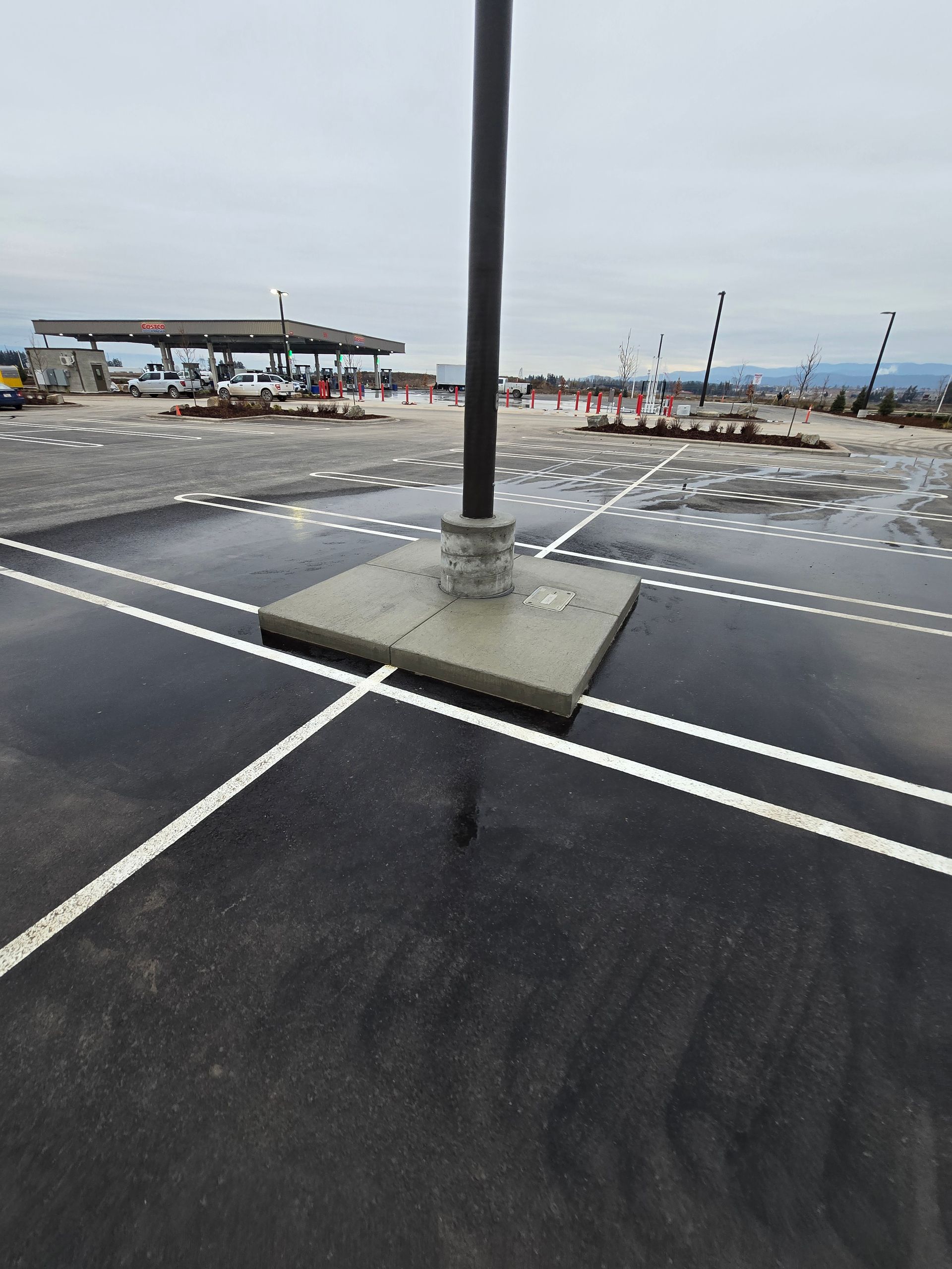 A light pole in the center of a paved parking lot with freshly painted white parking lines under an overcast sky.