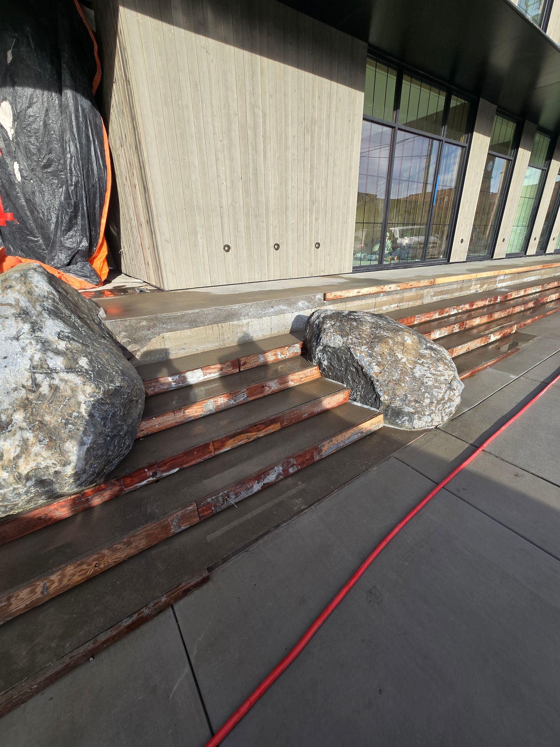 Large boulders block a set of outdoor concrete stairs leading to a building entrance, hindering pedestrian access.