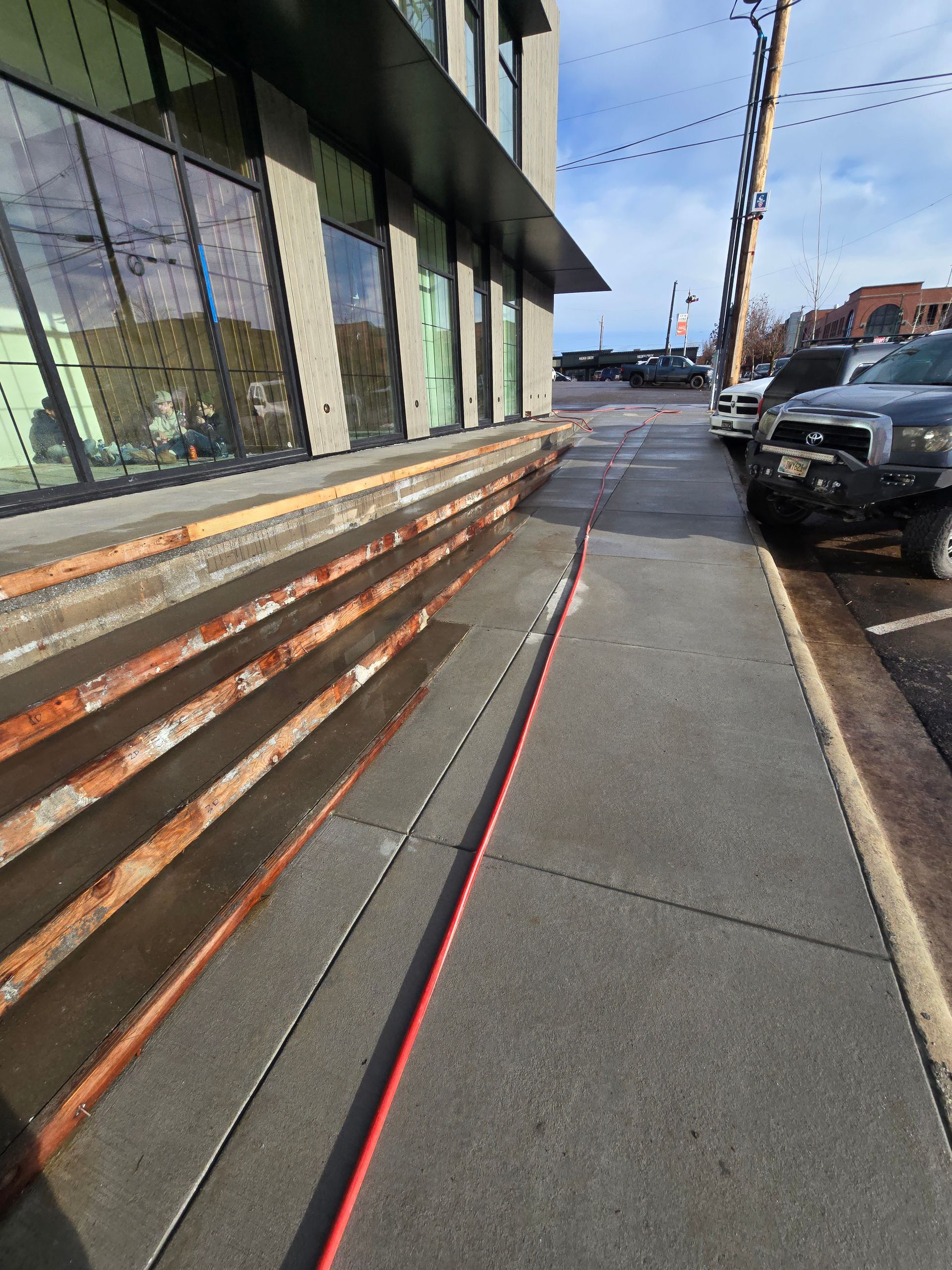 A long orange cord lies across a gray concrete sidewalk next to a building entrance with multiple steps.