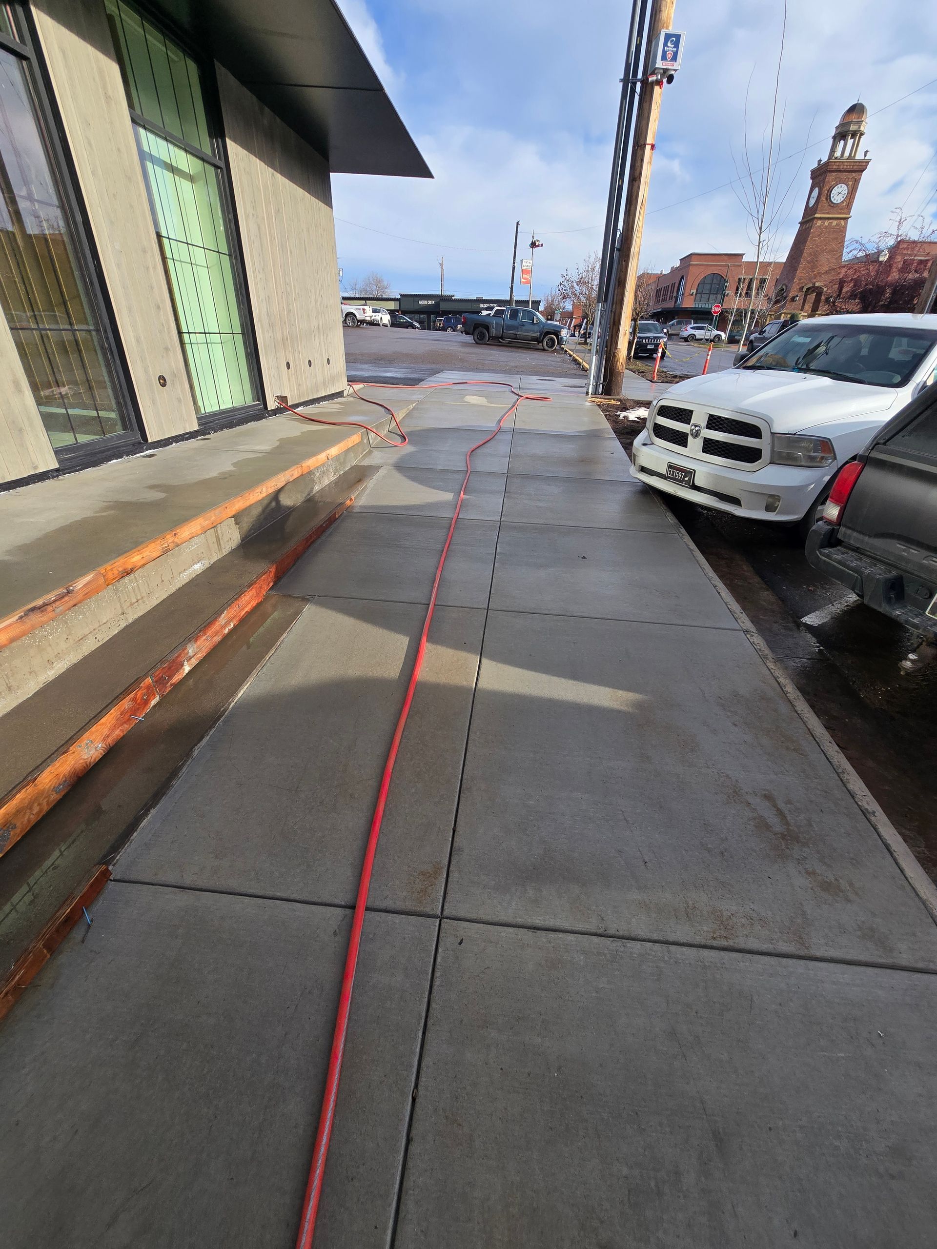 A red cable stretches across a gray concrete sidewalk next to a building and a parked white truck on a sunny day.