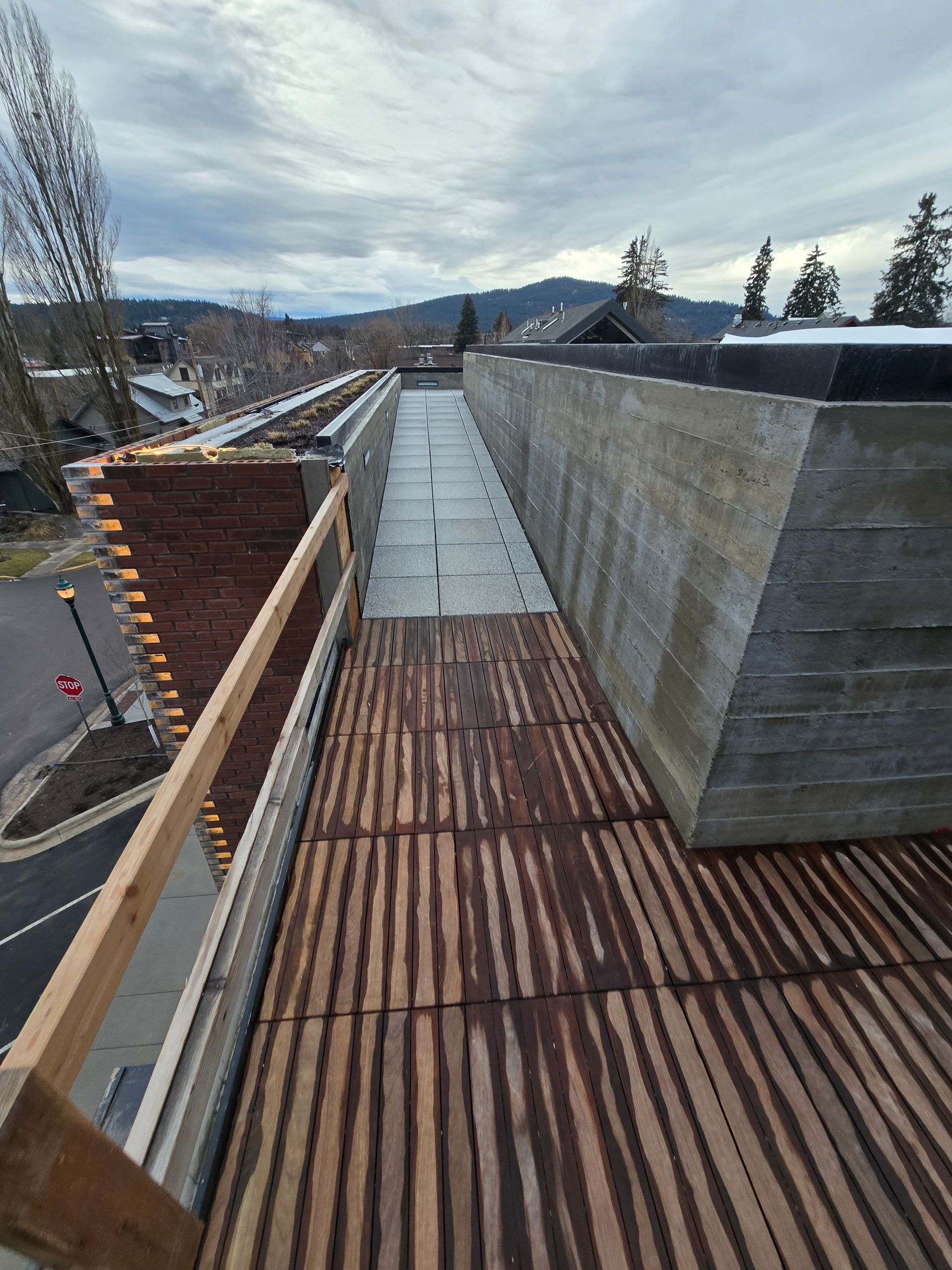 A wooden plank walkway runs between a brick wall with construction scaffolding and a tall, textured concrete wall.