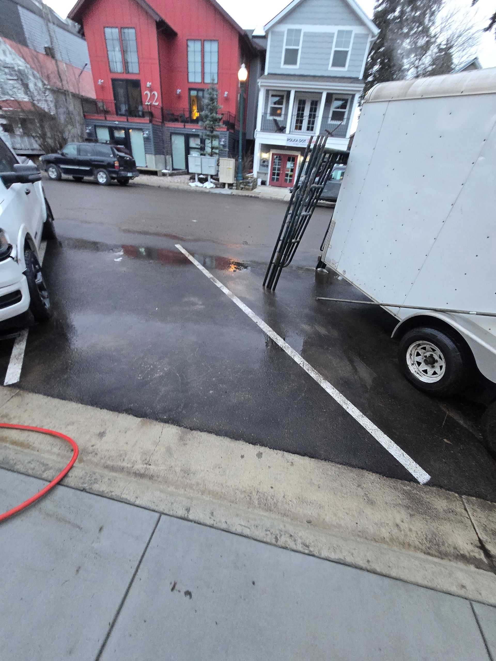 A parking space is blocked by a black metal ramp leaning against a white trailer, with a white truck parked to the left.