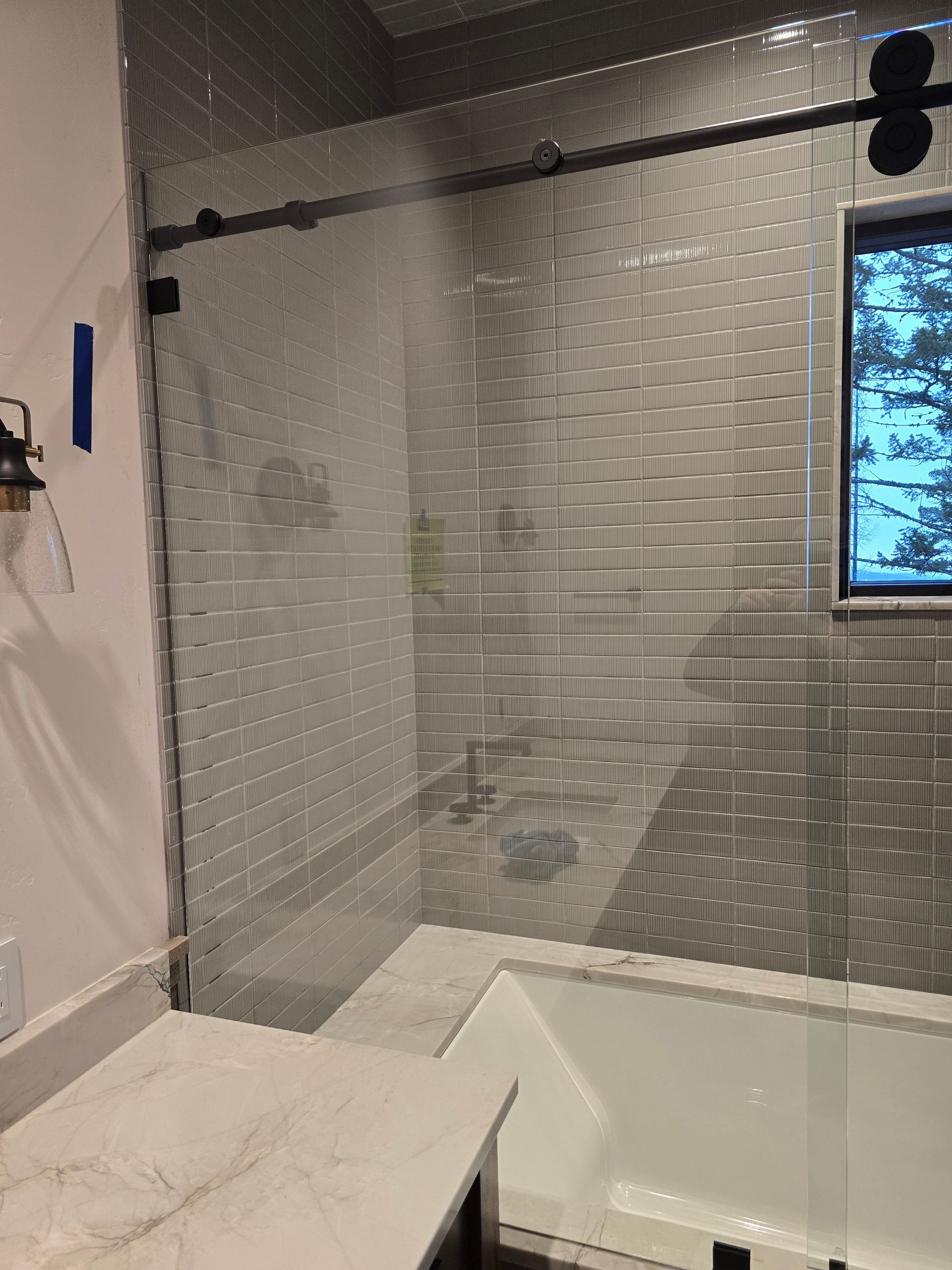 A modern bathroom featuring a glass shower door with black hardware, subway-tiled walls, and a white bathtub.