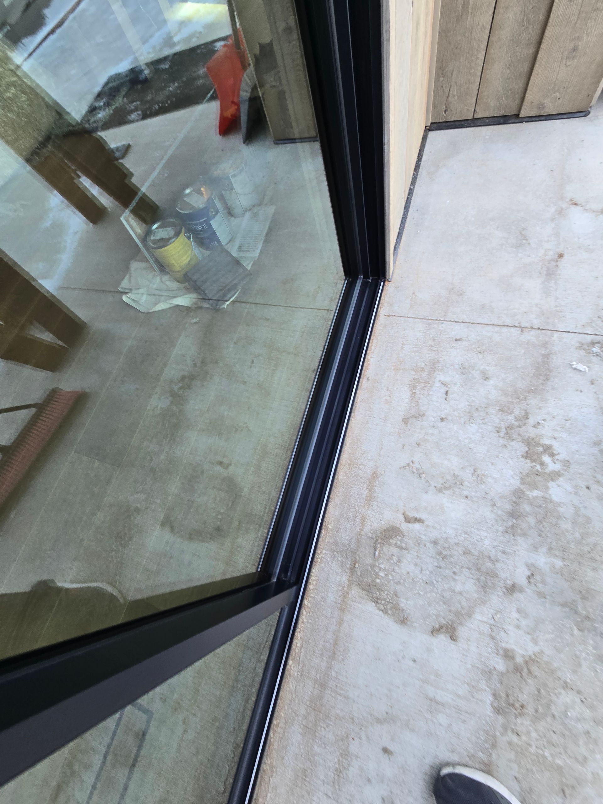 A high-angle view of a black sliding door frame installed against a light gray concrete floor and wood wall.