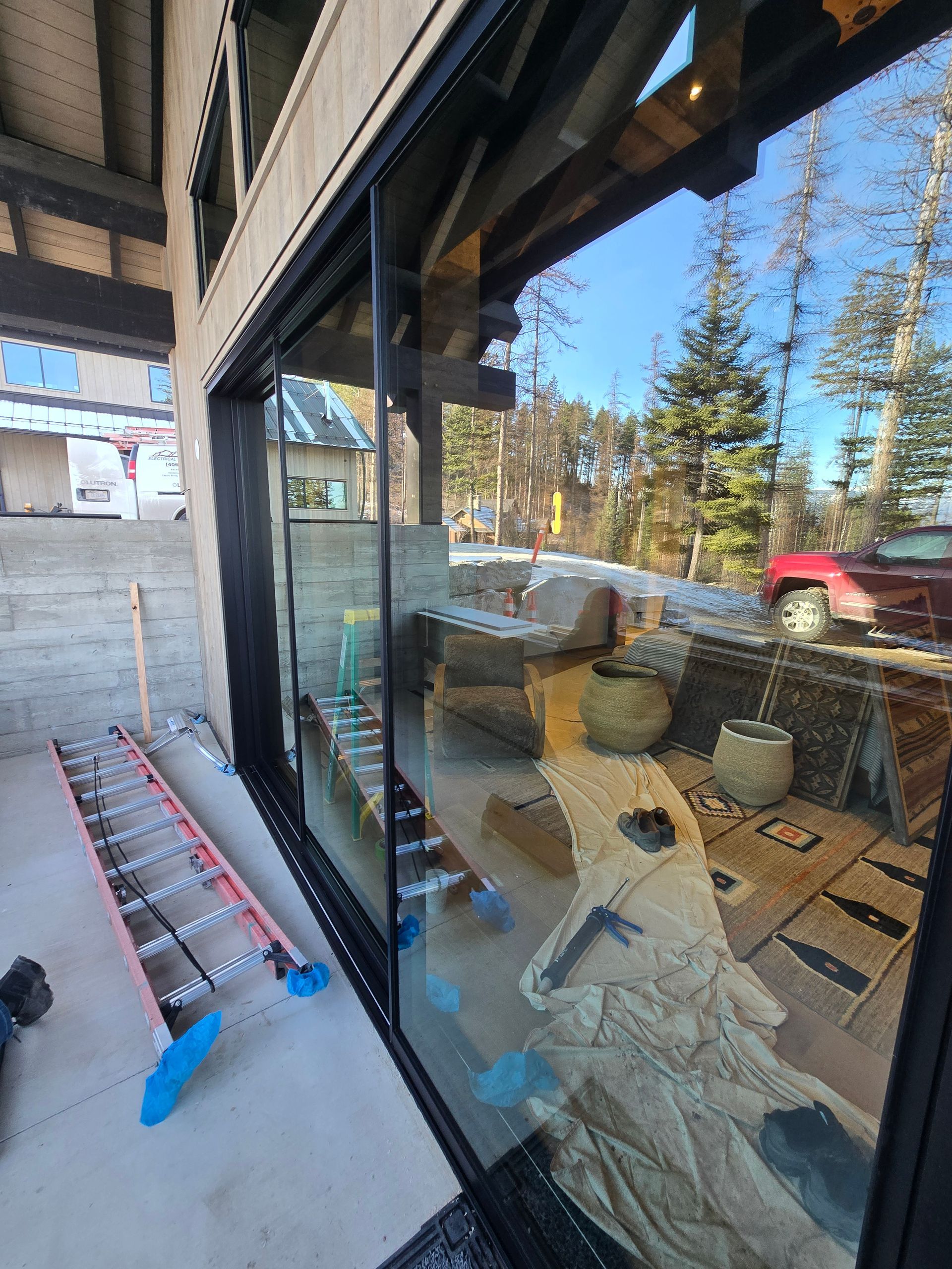 Large black-framed sliding glass doors reflecting an outdoor patio with a red truck, ladder, and construction materials.