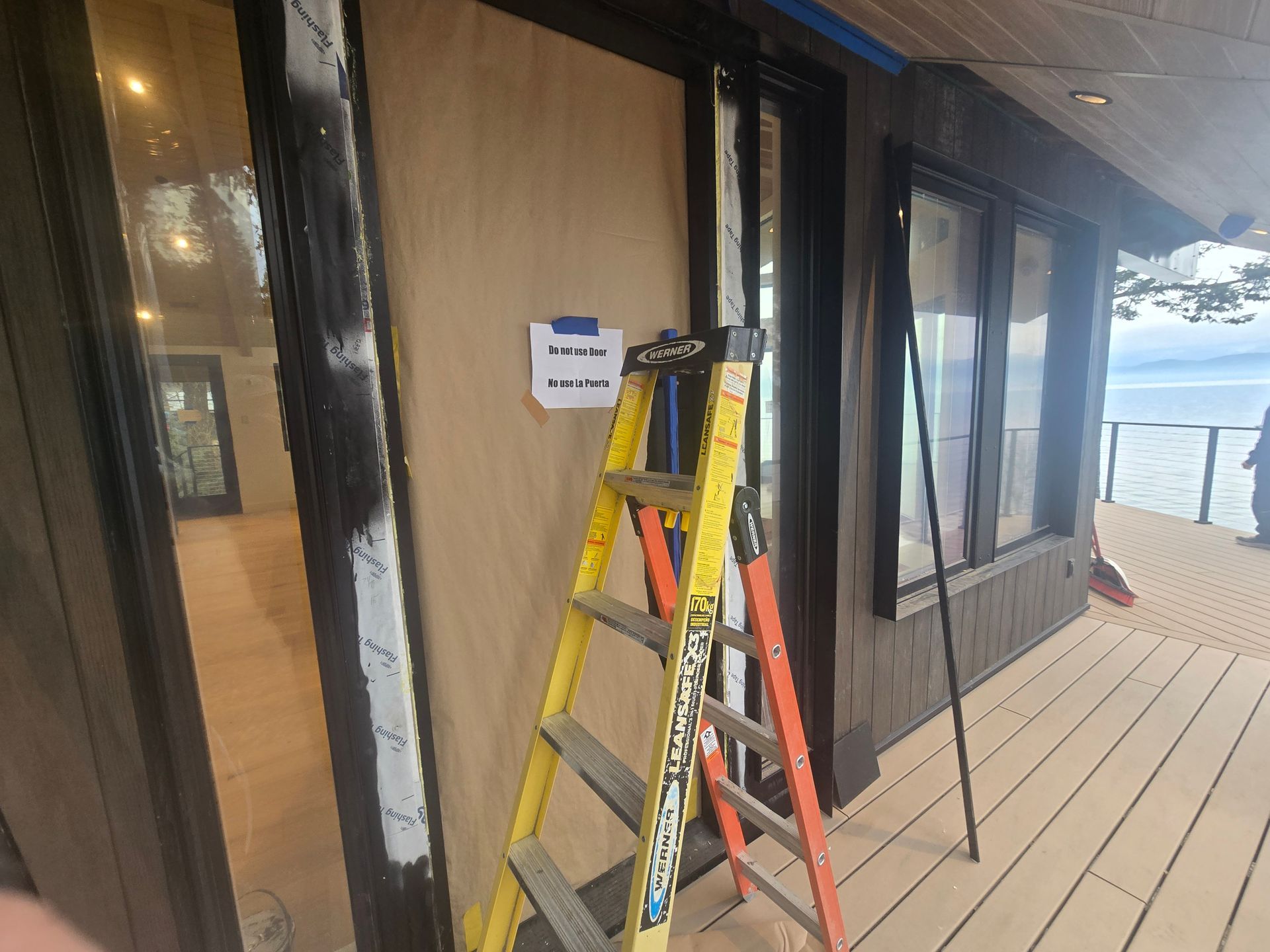 A yellow and orange step ladder stands on a deck in front of a building undergoing renovation with masked windows.