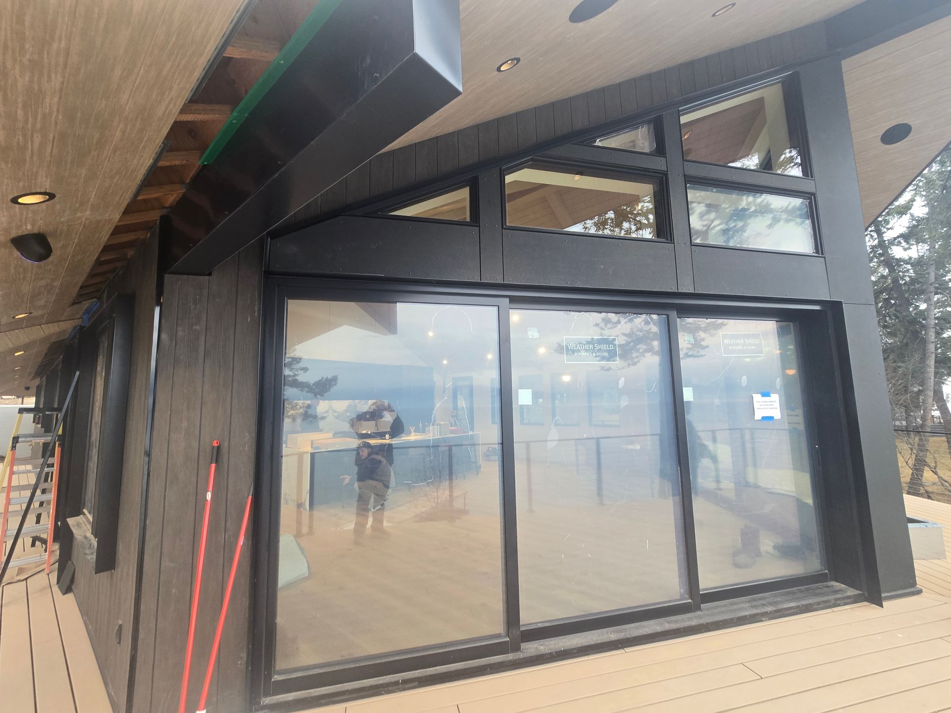 Modern home exterior with dark wood siding, large sliding glass doors, and triangular windows under an angled roof.
