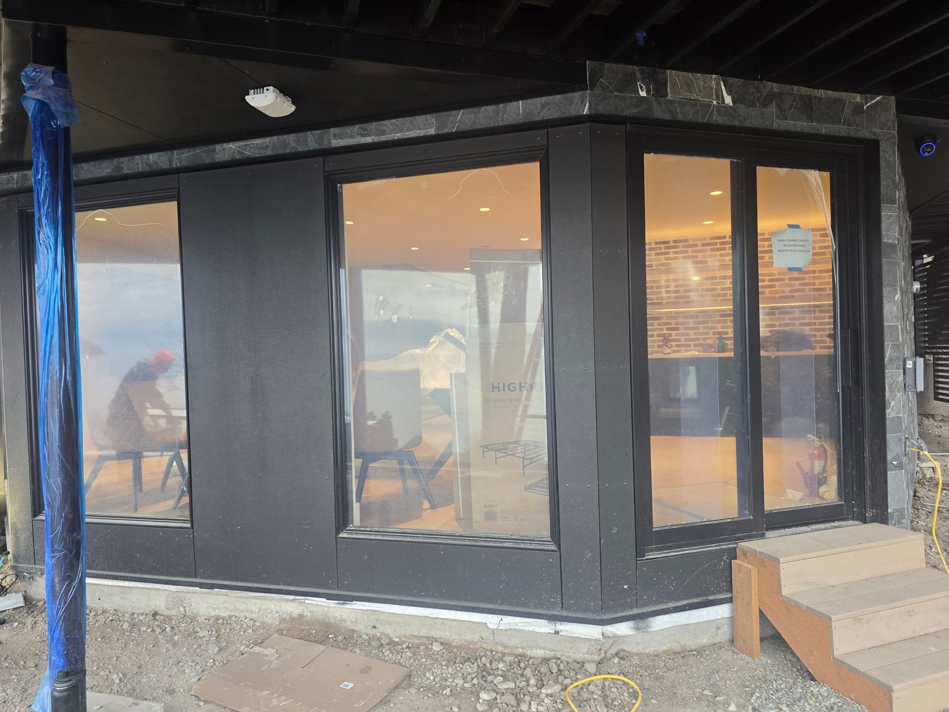 A modern exterior storefront featuring dark walls, large glass windows, and a set of wooden steps leading to the entrance.